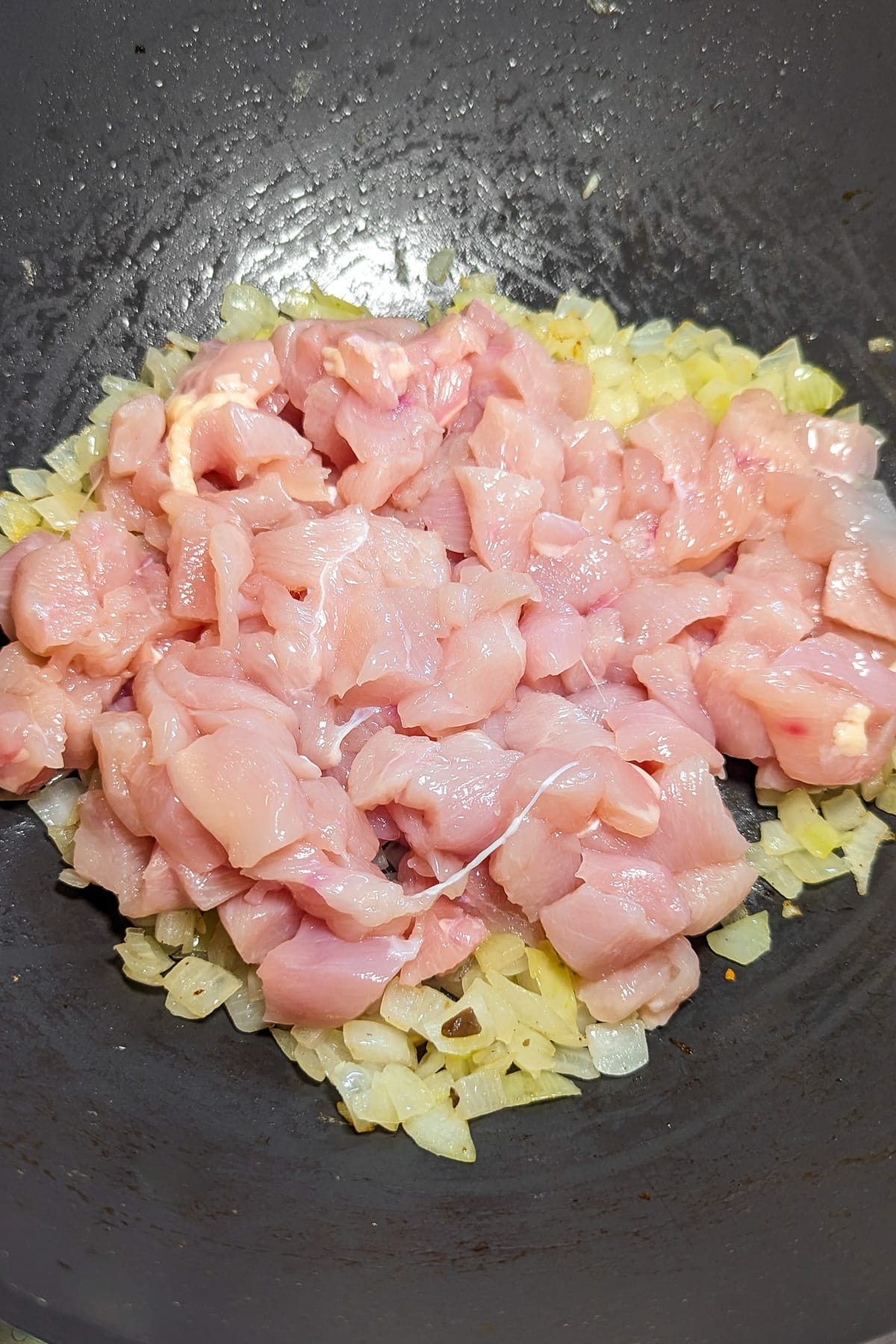 Raw chicken breasts over caramelized onions in a wok.