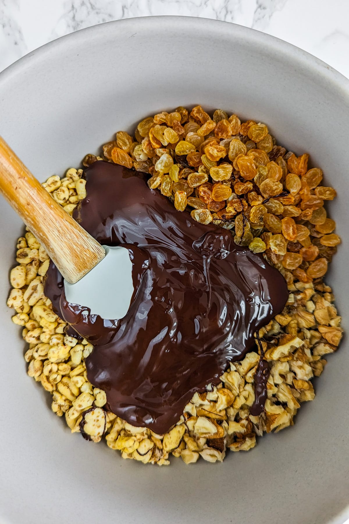 Large bowl with raisins, melted chocolate, walnuts and rice bubbles.