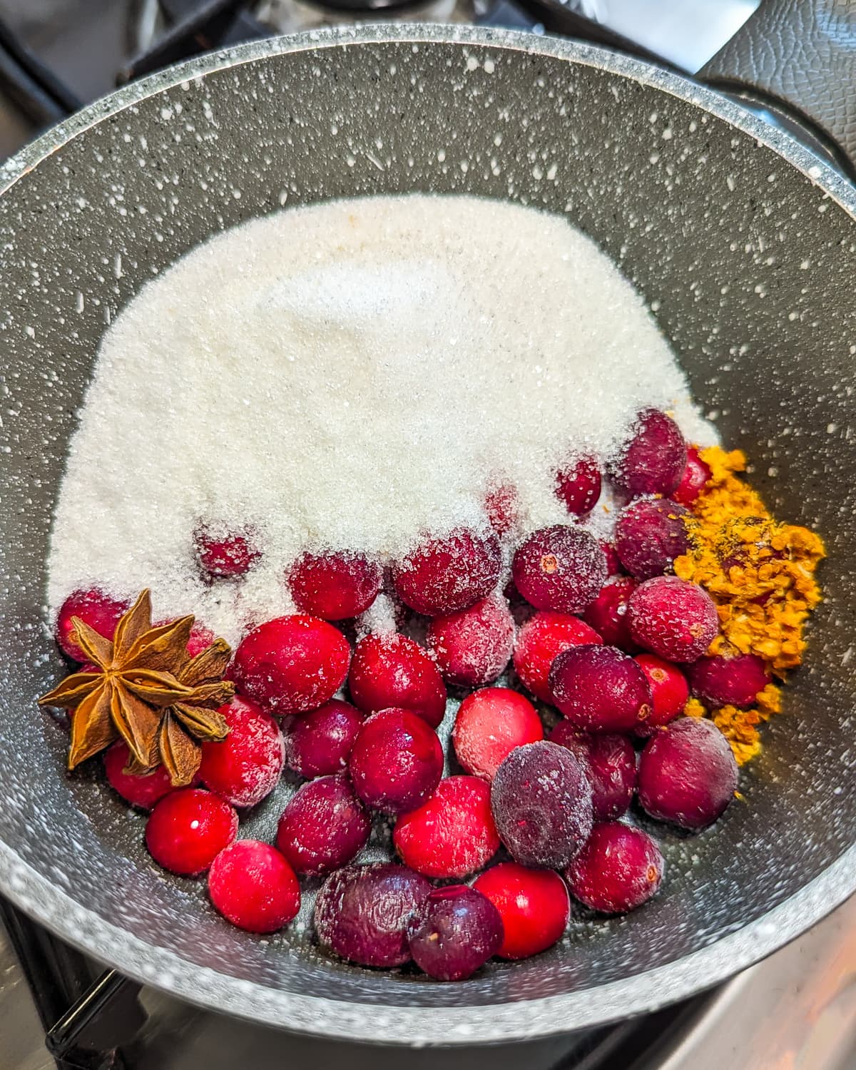 Frozen cranberries, star anice, dried orange peel and sugar in a pan on the stove.