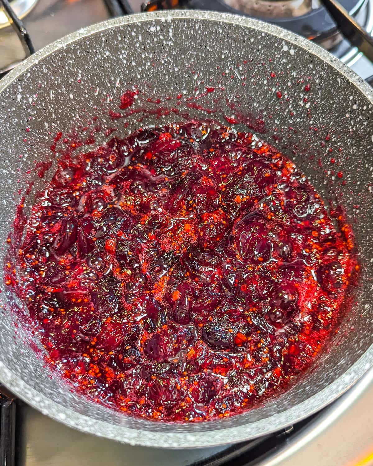 Christmas jam of cranberries boiling in a pan on the stove.