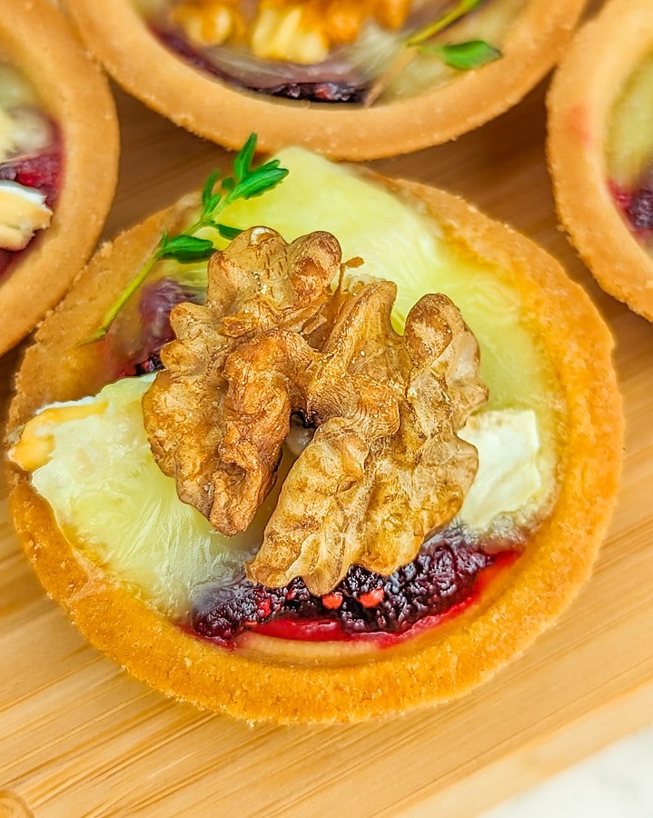 Cranberry and brie bites with walnuts on a wooden serving board.