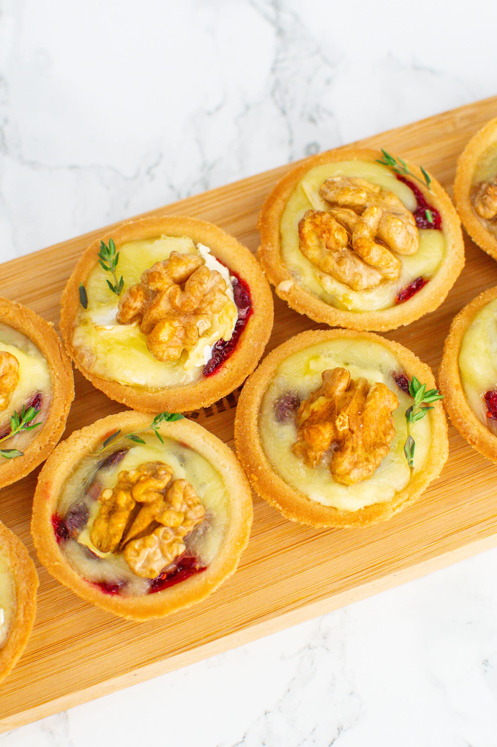 Wooden serving board with tartlets with brie cheese, walnuts and jam.