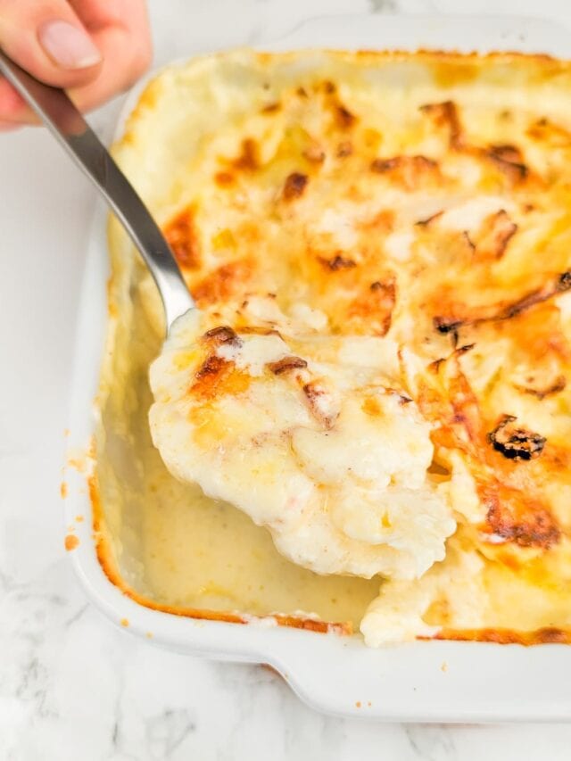 Woman hand with a spoon holding cauliflower gratin over a traybake.