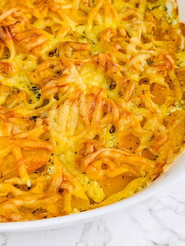 White casserole with cheesy pumpkin gratin on a white marble table.