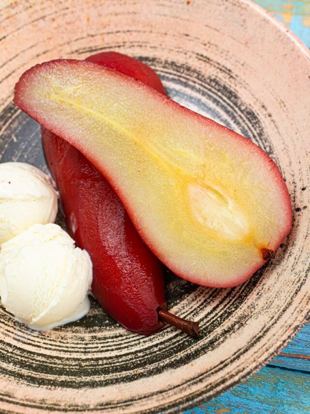 Poached pear halves near ice cream in a vintage plate on a blue wooden table.