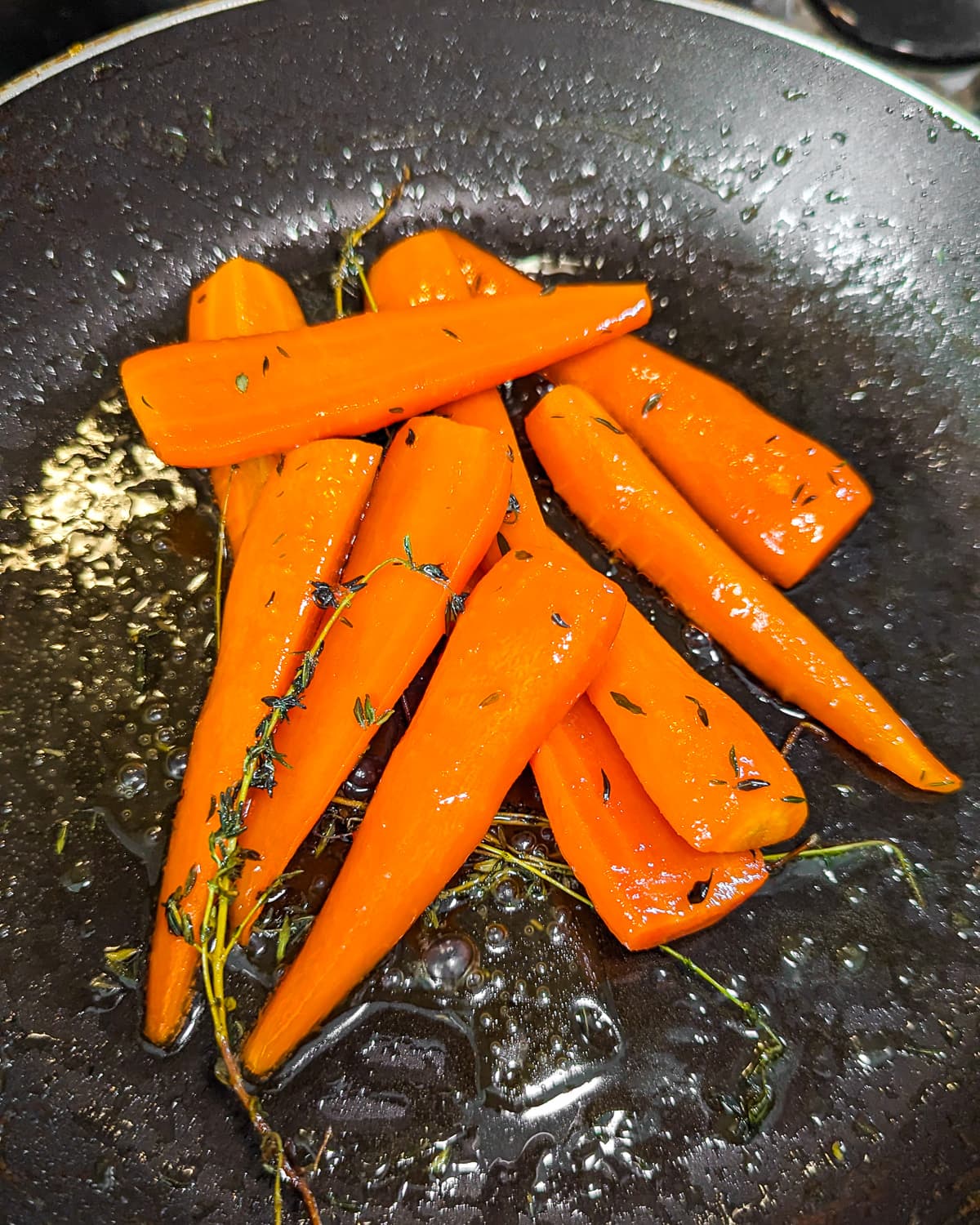 Caramelizing carrots in a frying pan with butter and thyme.