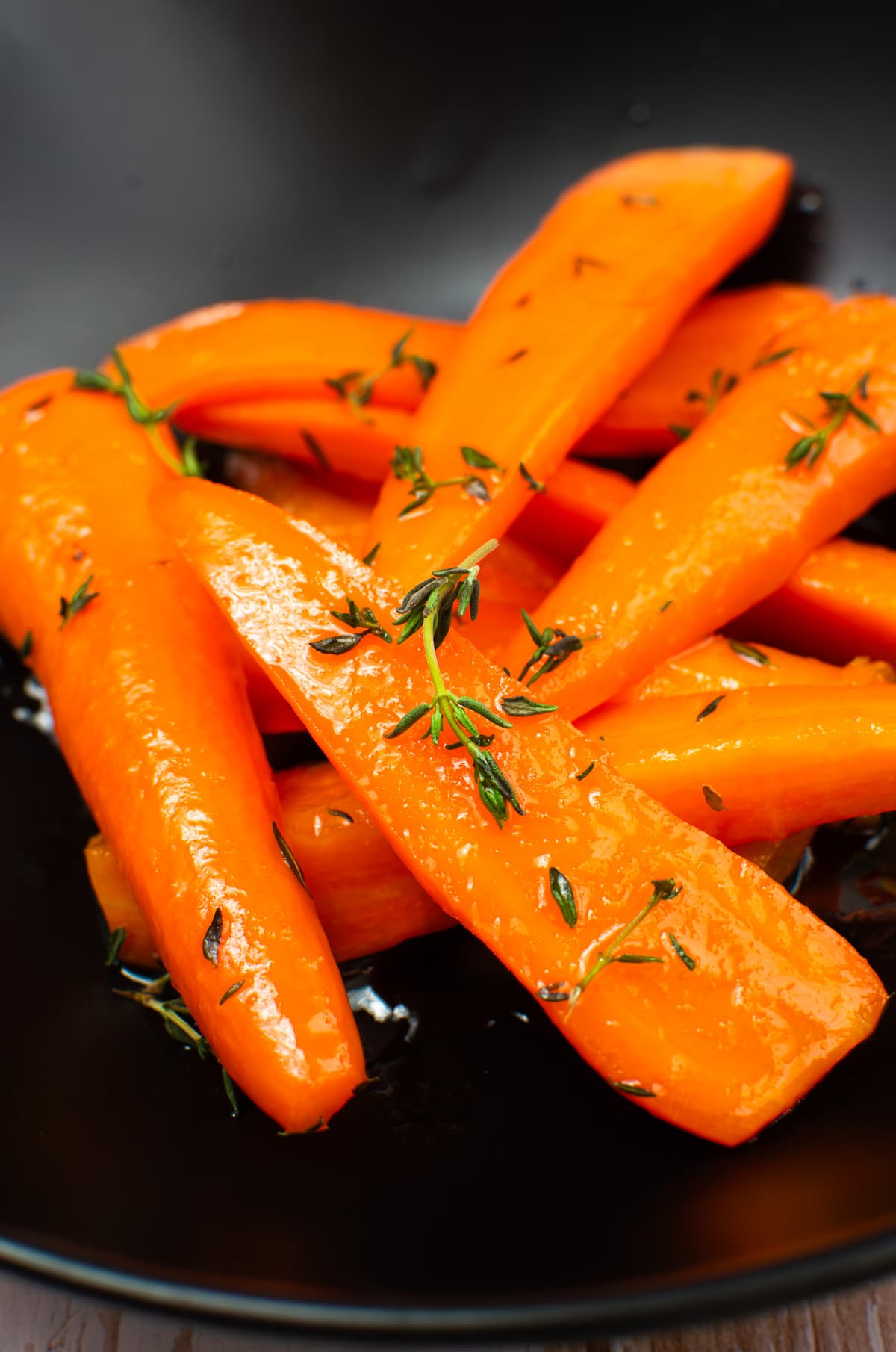 Glazed carrots with thyme in a black plate.