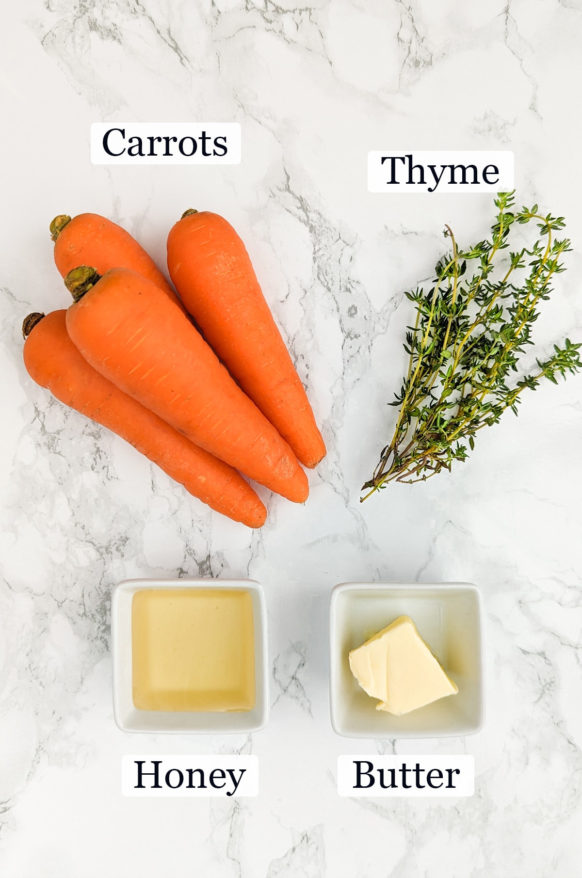 Carrots, thyme, honey, and butter on a white marble table.