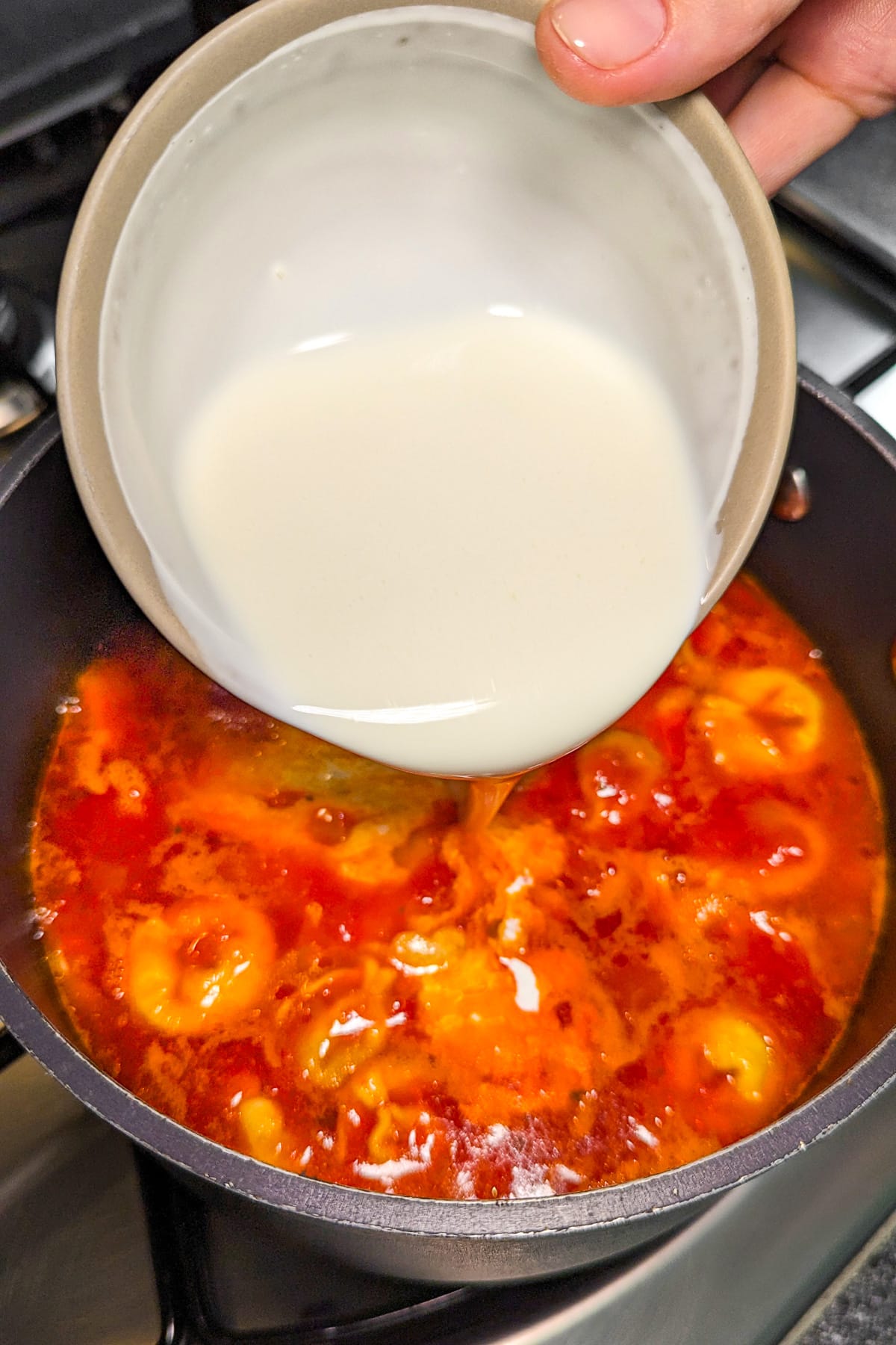 Pouring cream over a tomato soup in a pan on the stove.
