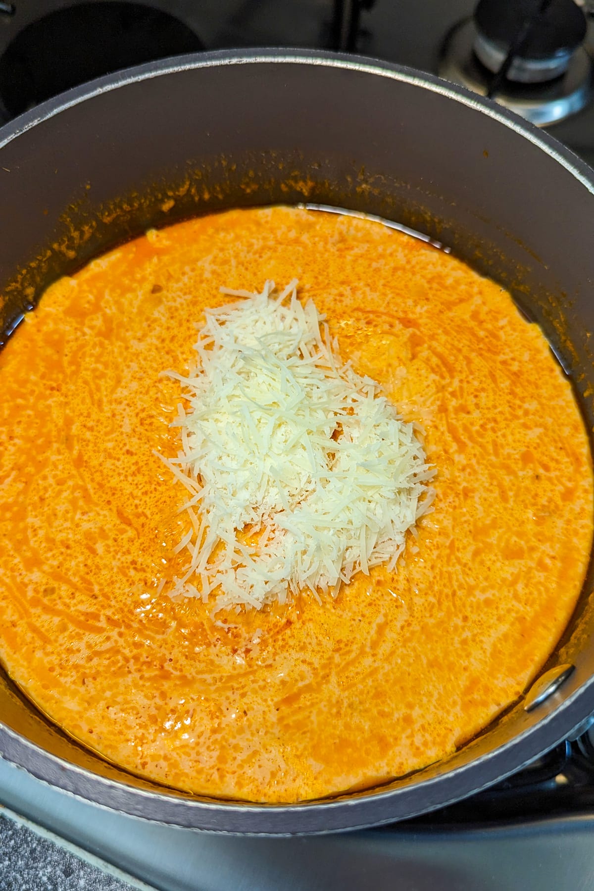 Shredded parmesan over a tomato soup in a pan on the stove.