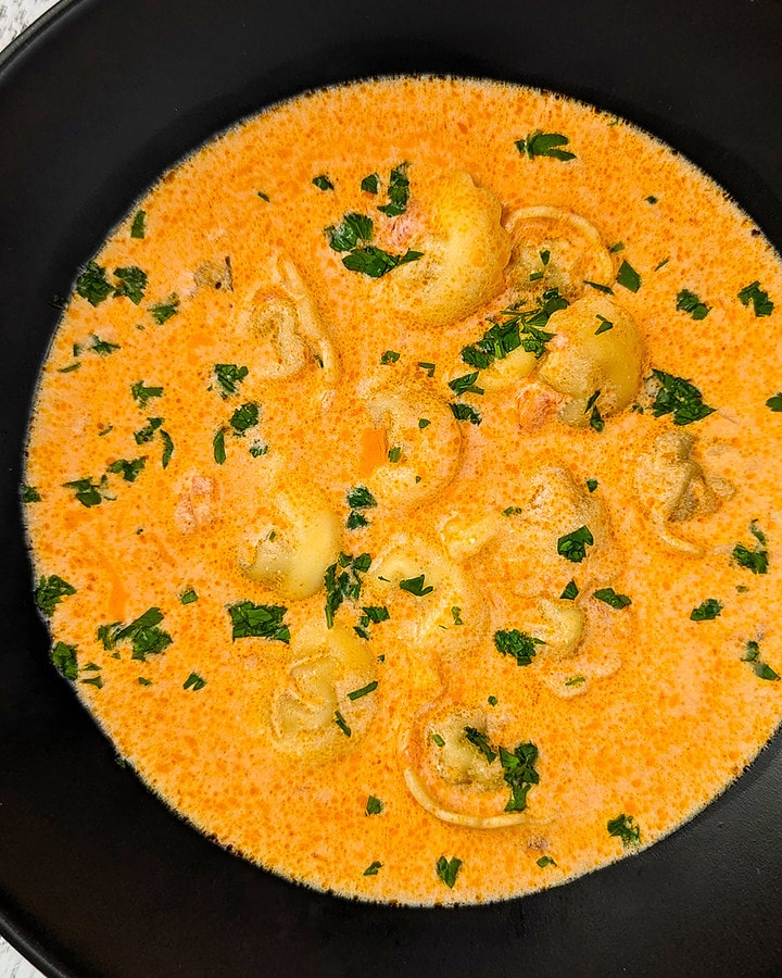 Creamy parmesan tomato soup with tortellini and chopped parsley.