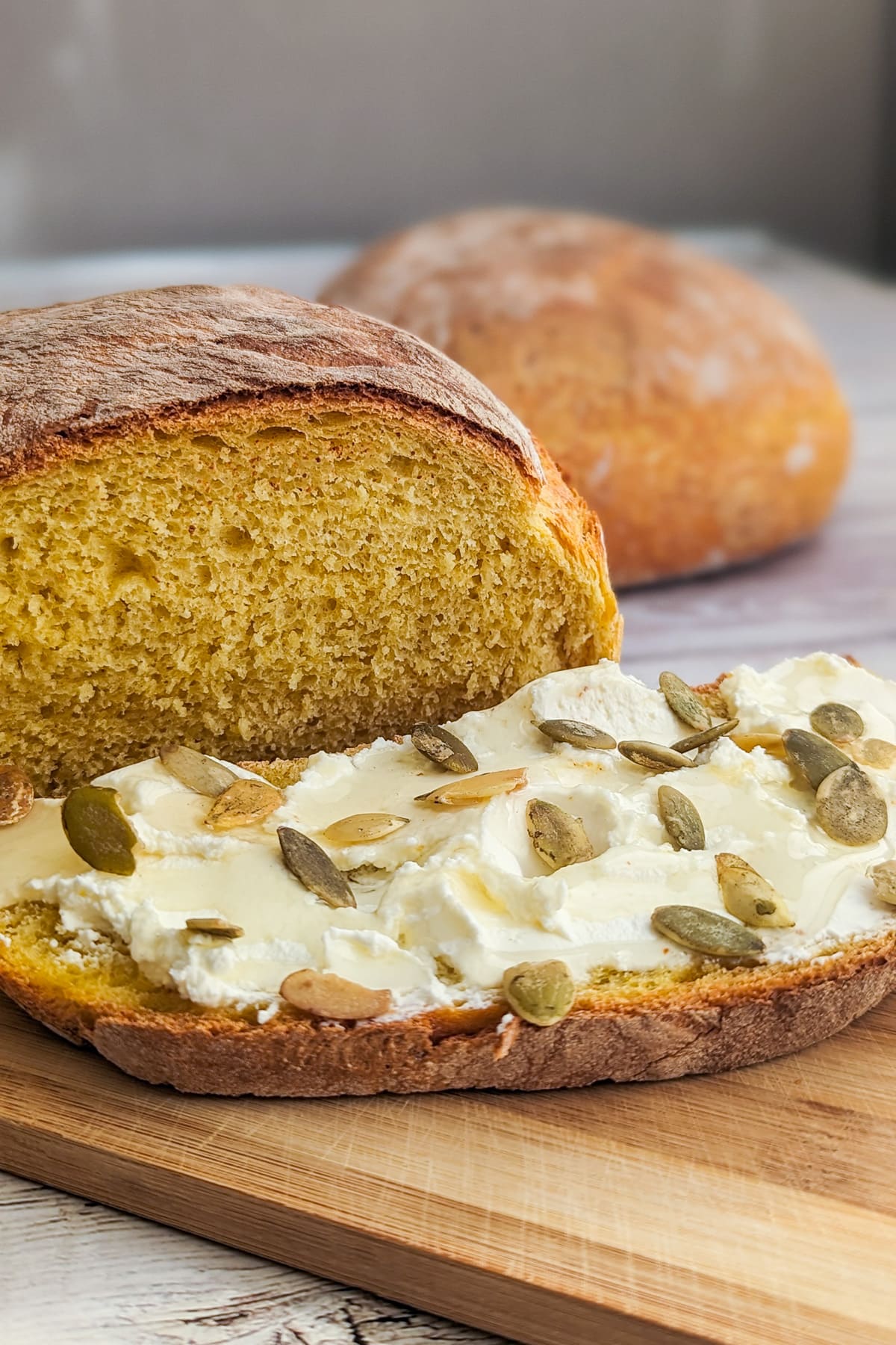 Slice of bread with cream cheese and pumpkin seeds on a wooden cutting board.
