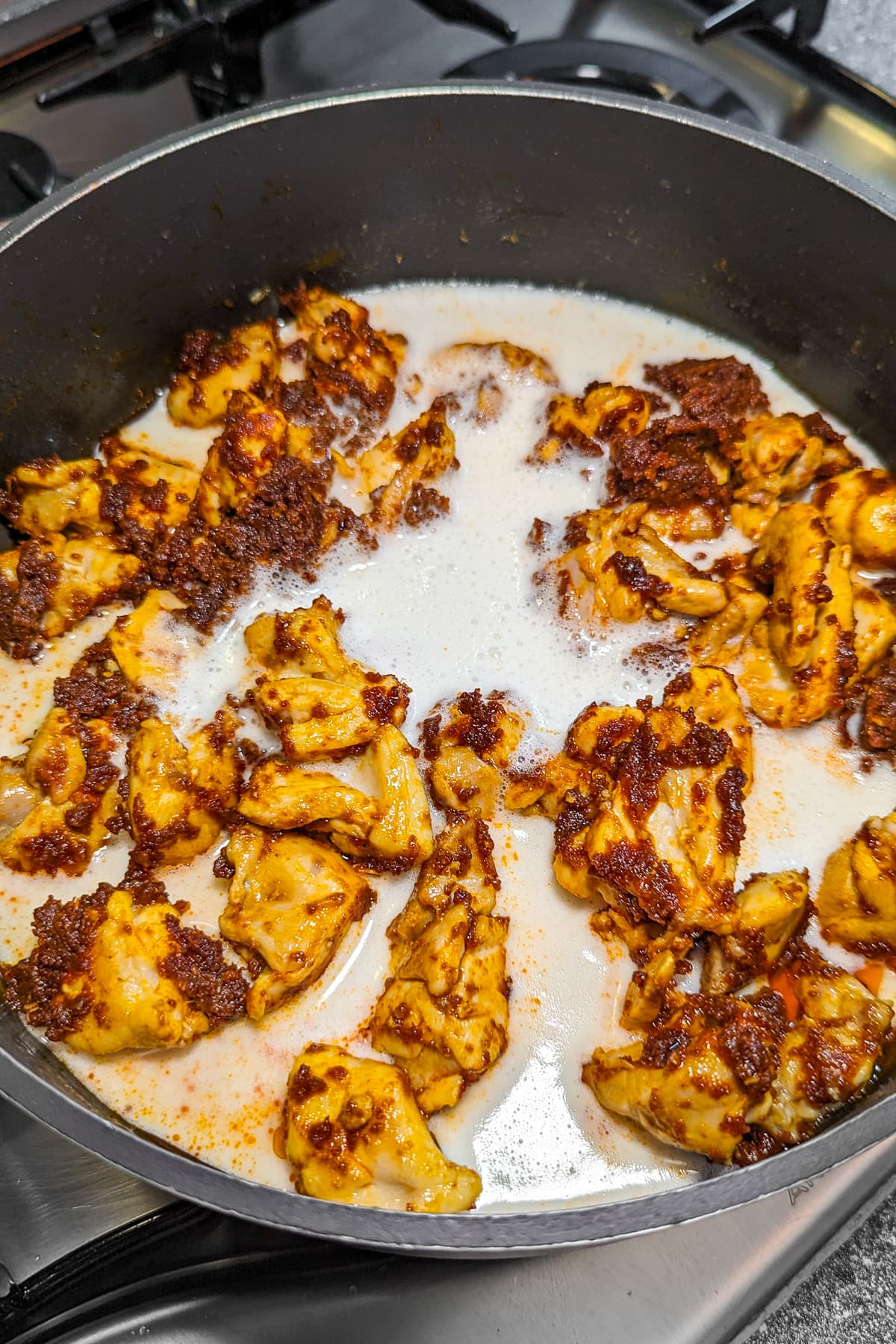 Adding milk over fried meat in a pan on the stove.