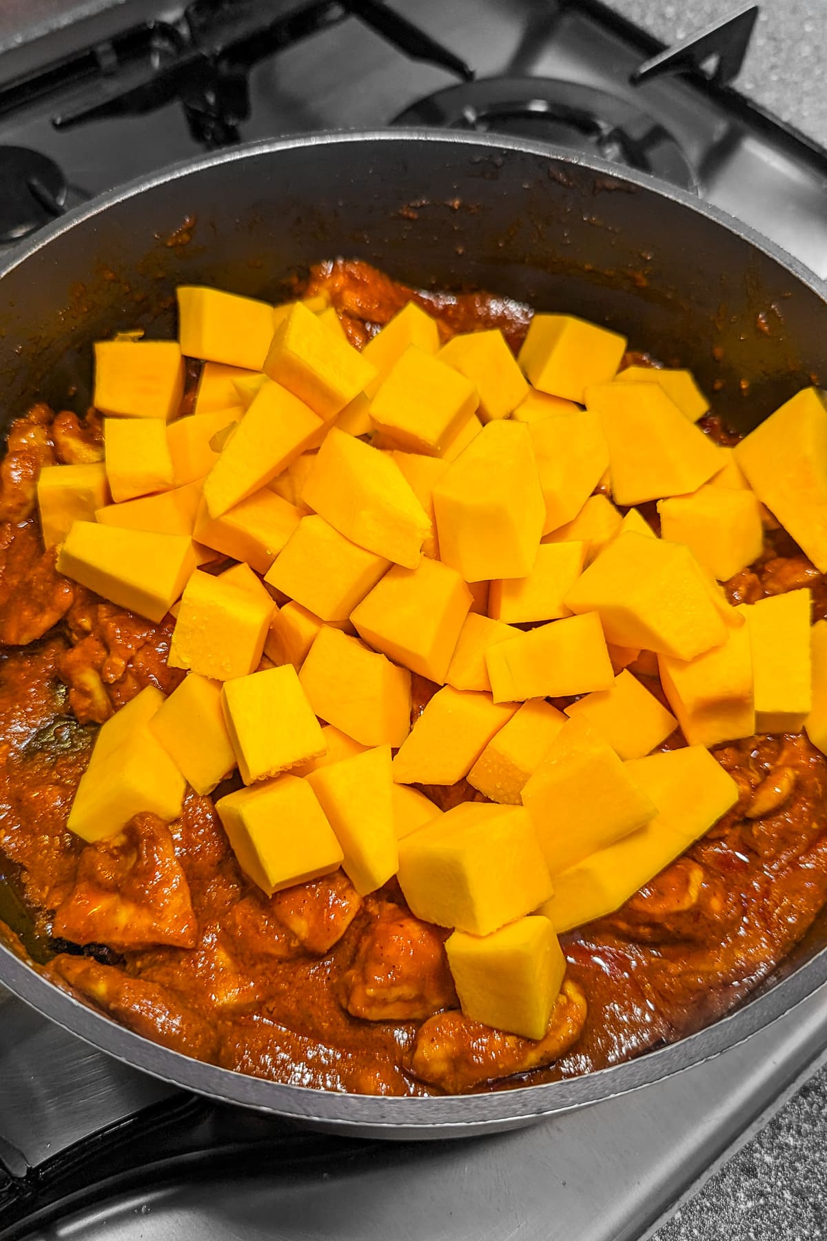 Adding pumpkin cubes over meat pieces in a pan on the stove.