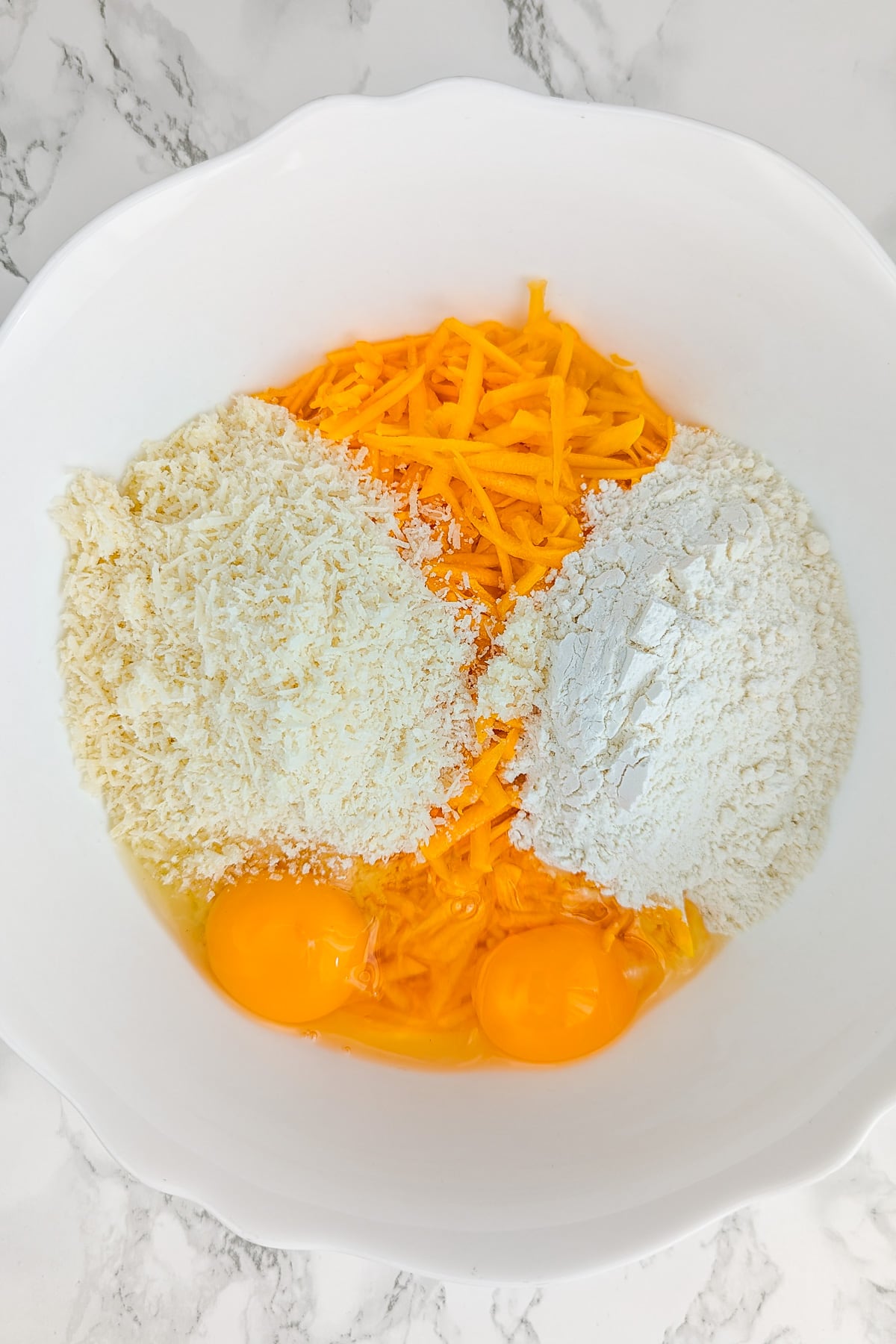 Grated pumpkin, eggs, parmesan and flour in a large white bowl.