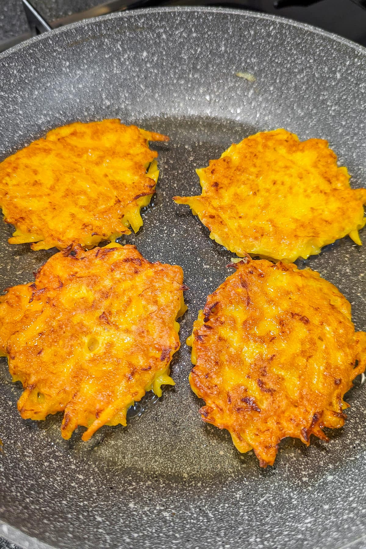 4 pumpkin fritters in a frying pan on the stove.