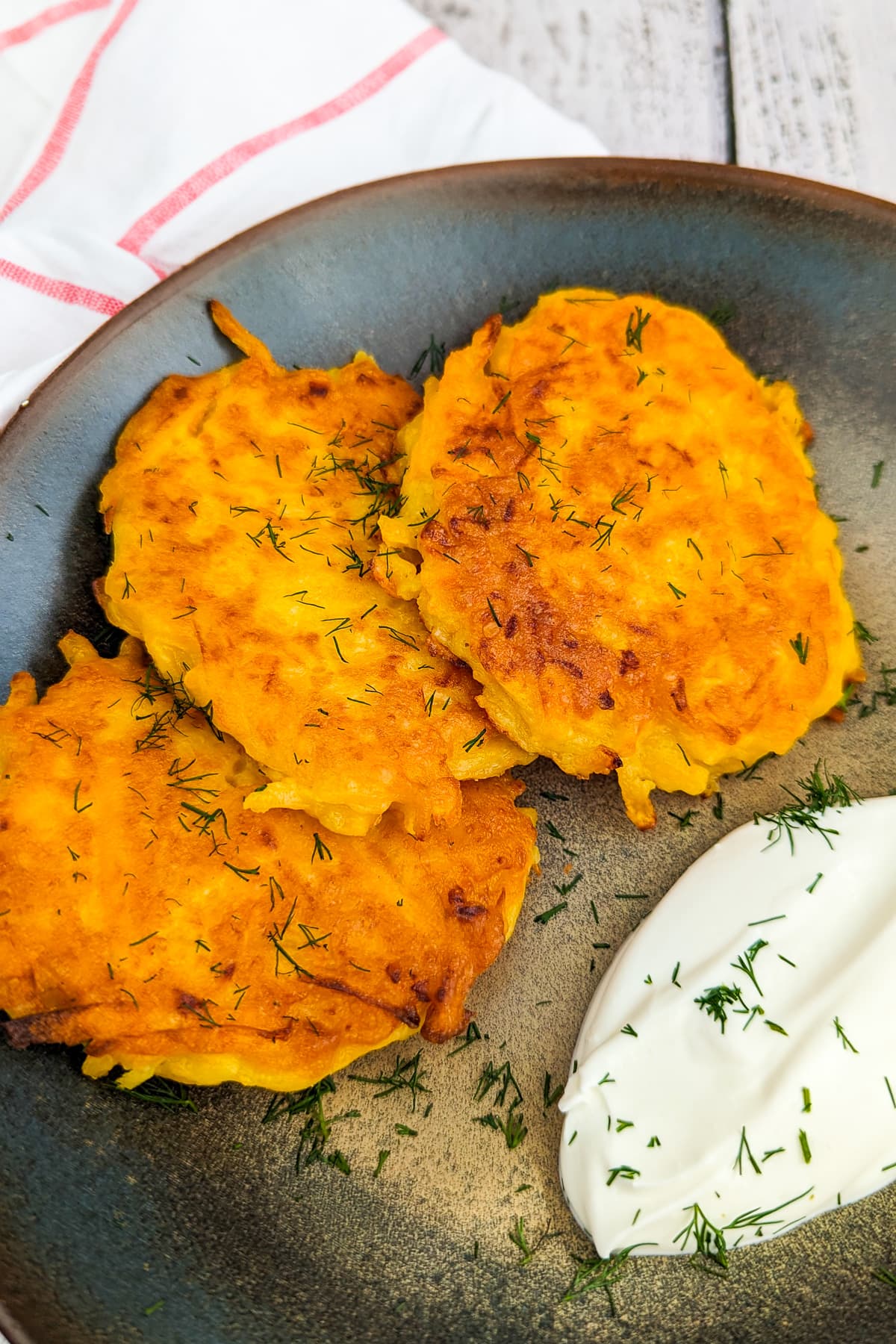 3 pumpkin fritters with sour cream, dill in a vintage plate on a wooden table.