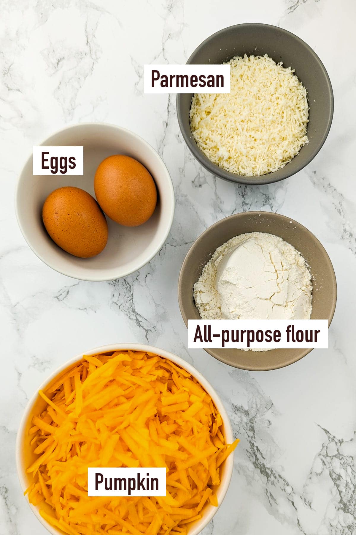 A plate with grated pumpkin, flour, parmesan and two eggs on a white marble table.