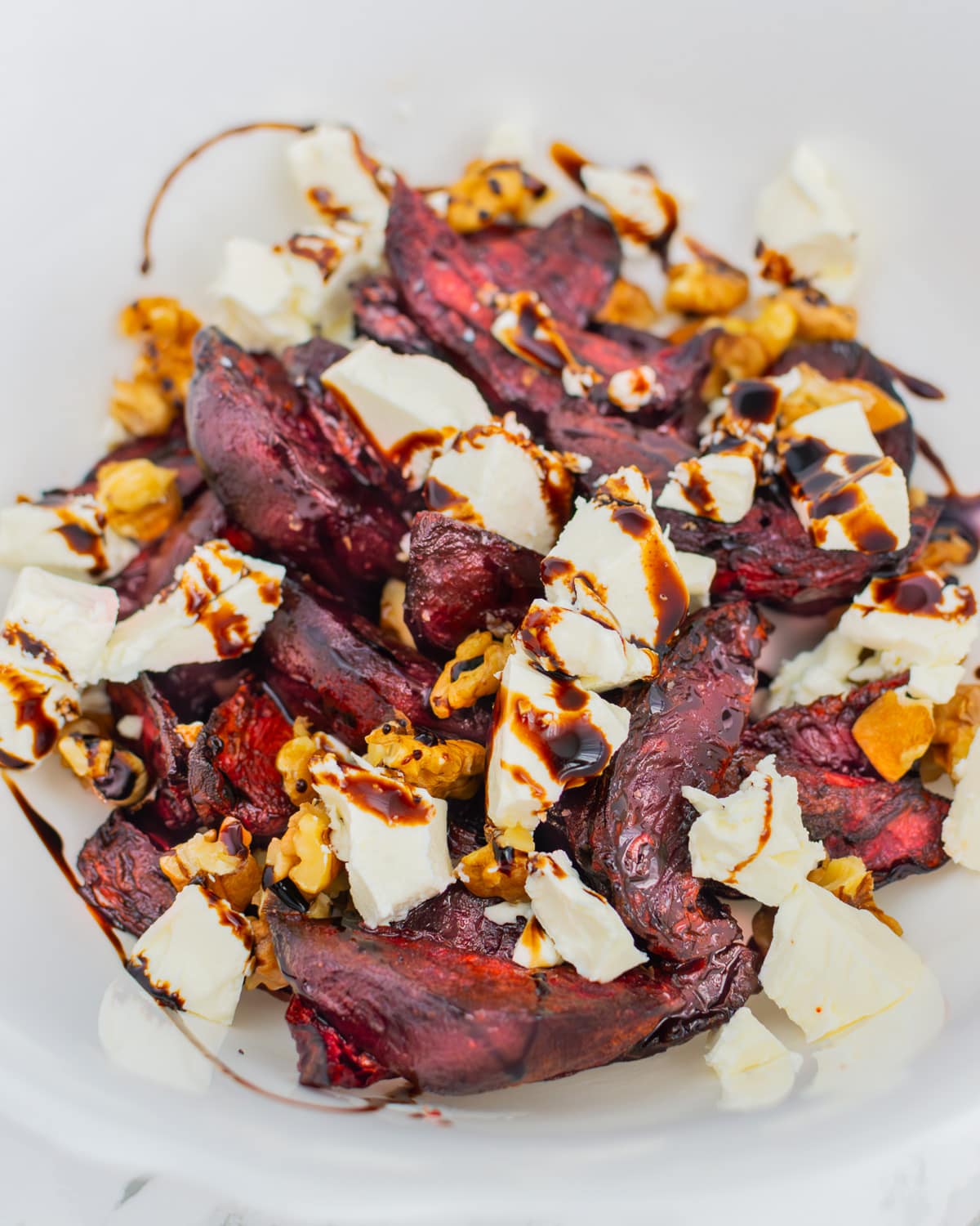 White deep bowl with roasted beet wedges, brie cheese, balsamic glaze and walnuts.