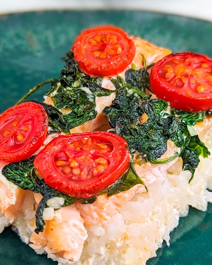 A slice of salmon baked rice with spinach and tomatoes in a green plate.