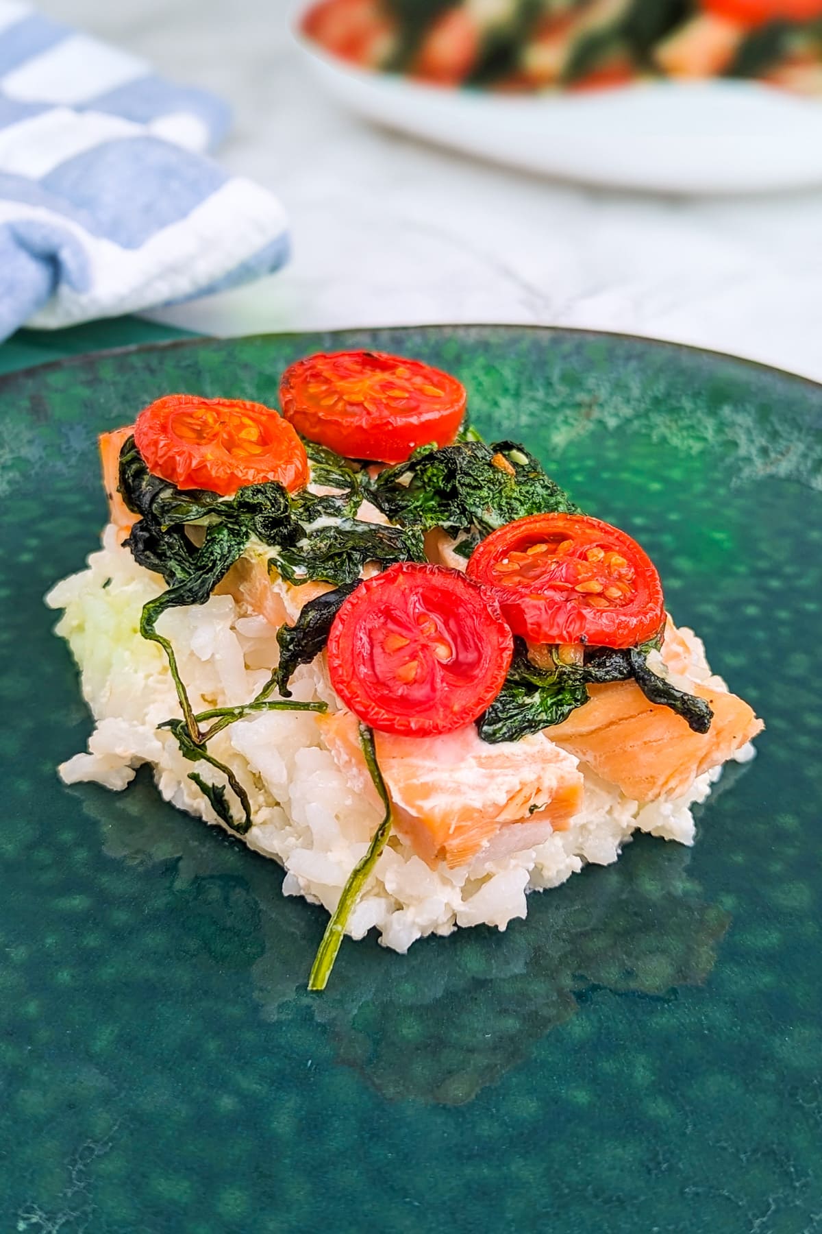 A slice of salmon baked rice with spinach and tomatoes in a green plate.