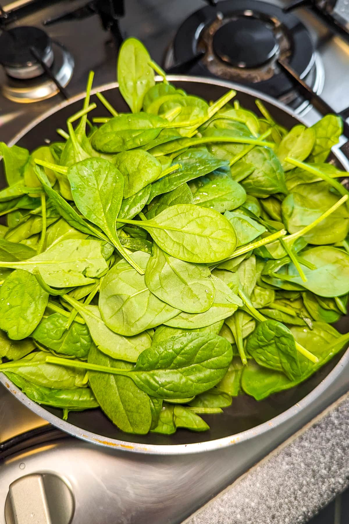 A bunch of fresh spinach in a frying pan on the stove.