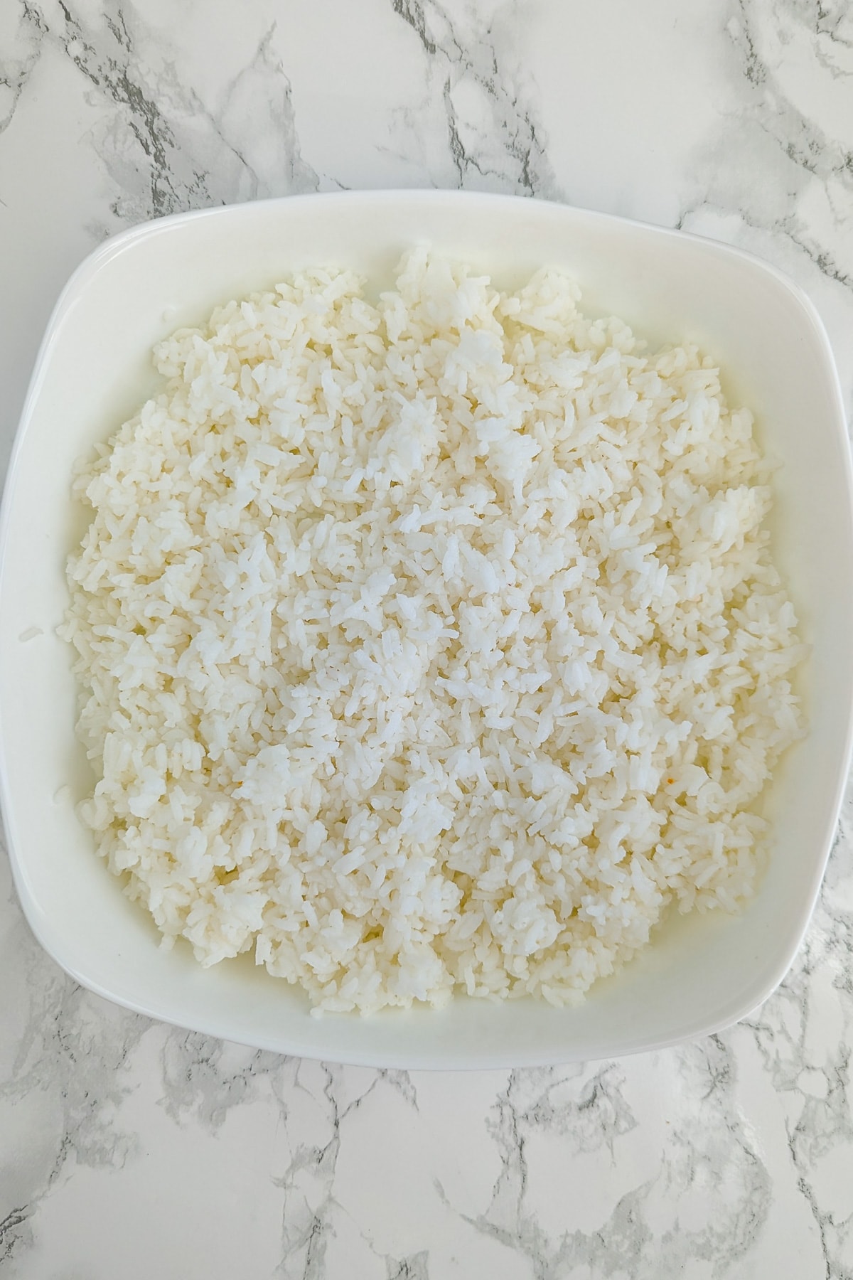 White casserole full with leftover boiled rice sitting on a white marble table.