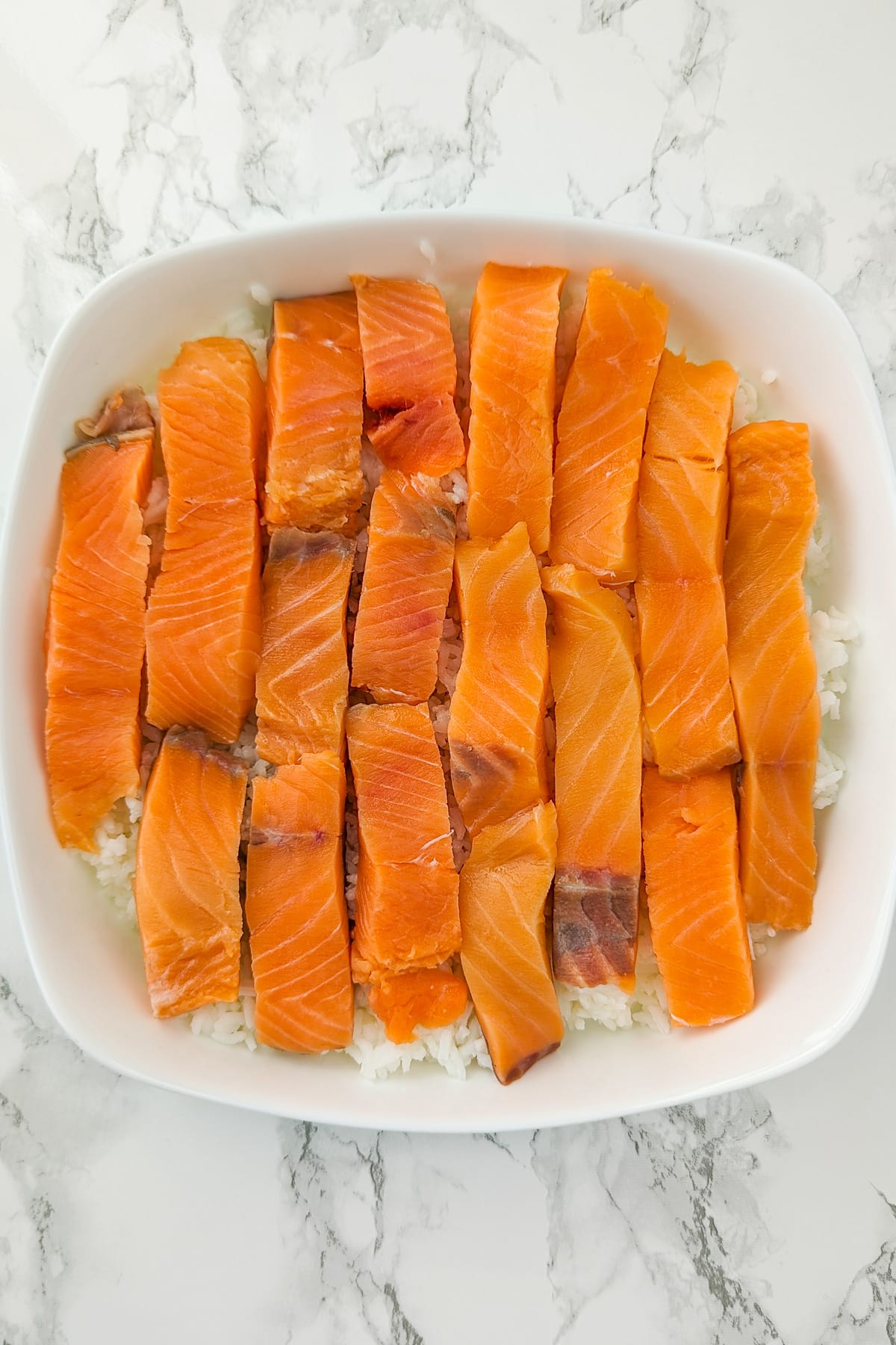 A casserole with boiled rice and covered with salmon slices.
