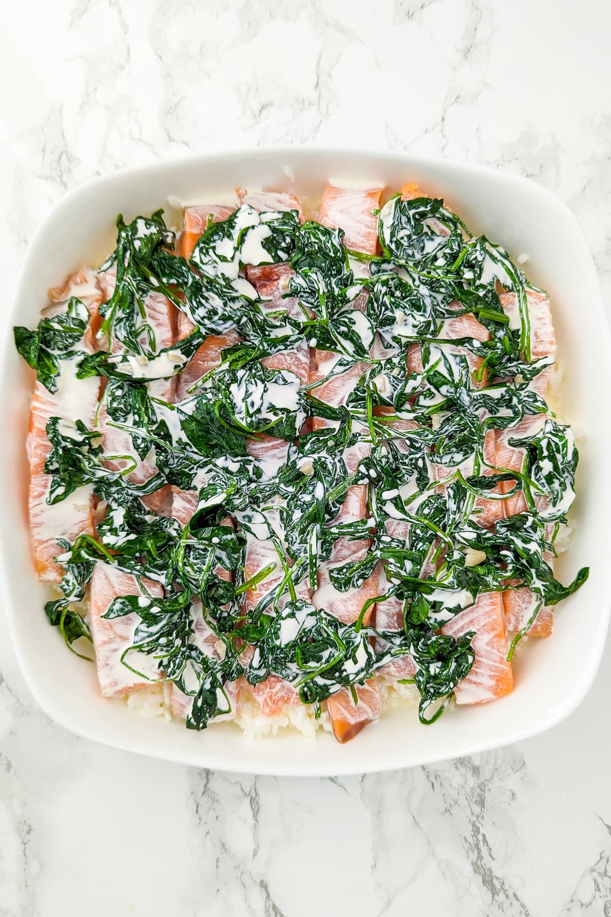 White casserole with boiled rice, salmon slices, cooked spinach and cream.