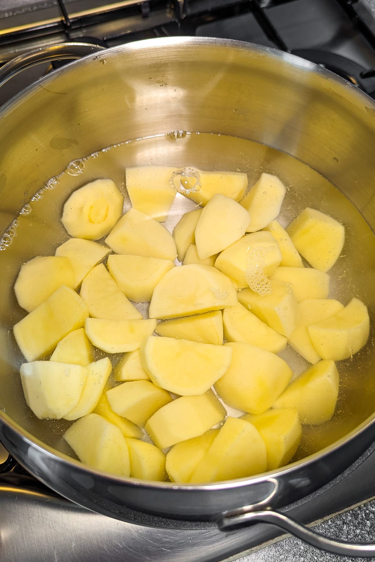 A pan with pototo chunks boiling in the water.