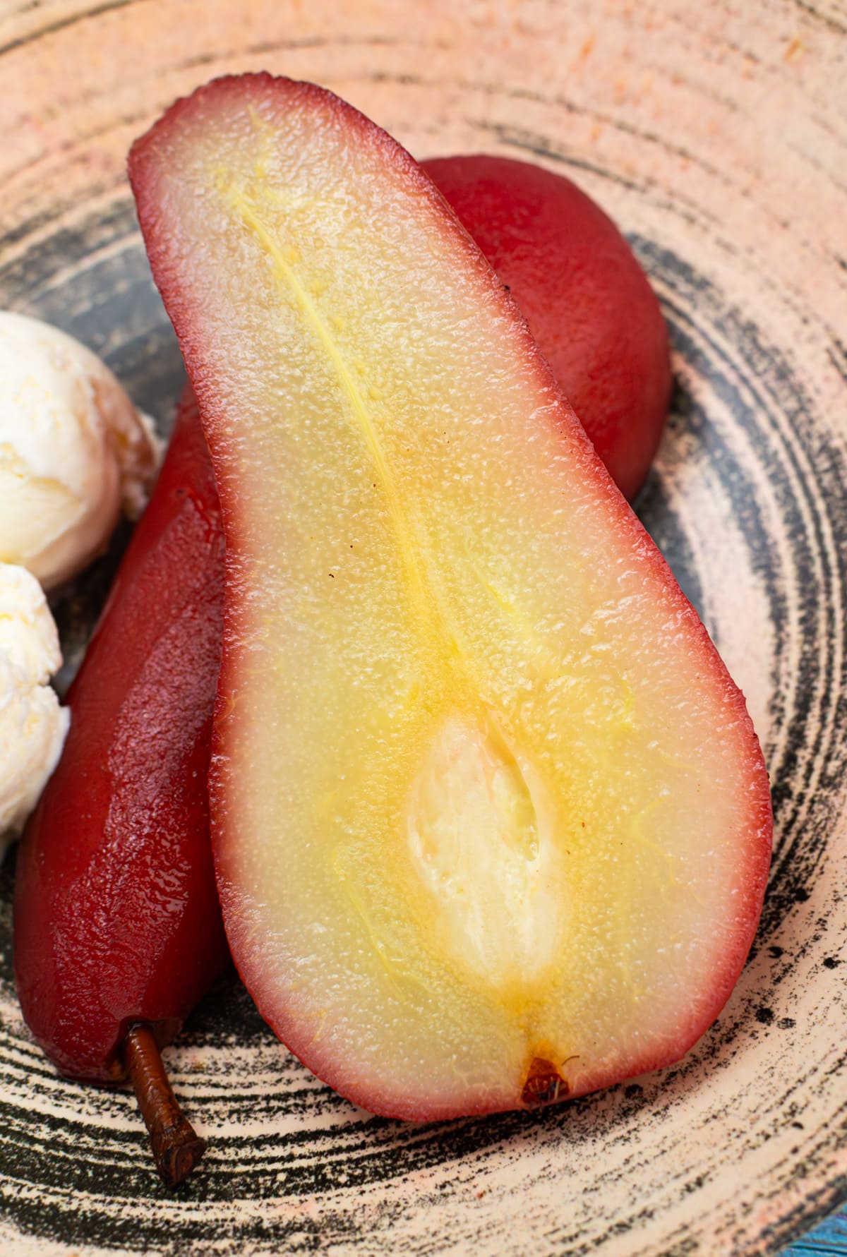 Poached pear halves near ice cream in a vintage plate on a blue wooden table.