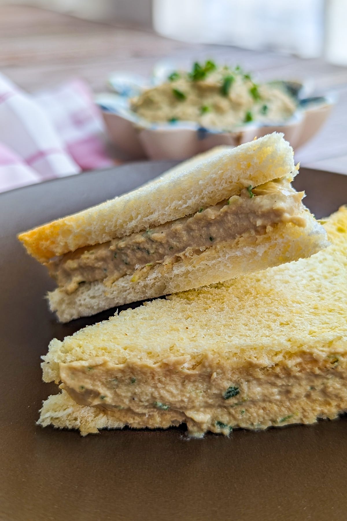 Close look of 2 sandwiches of tuna spread on a brown plate.