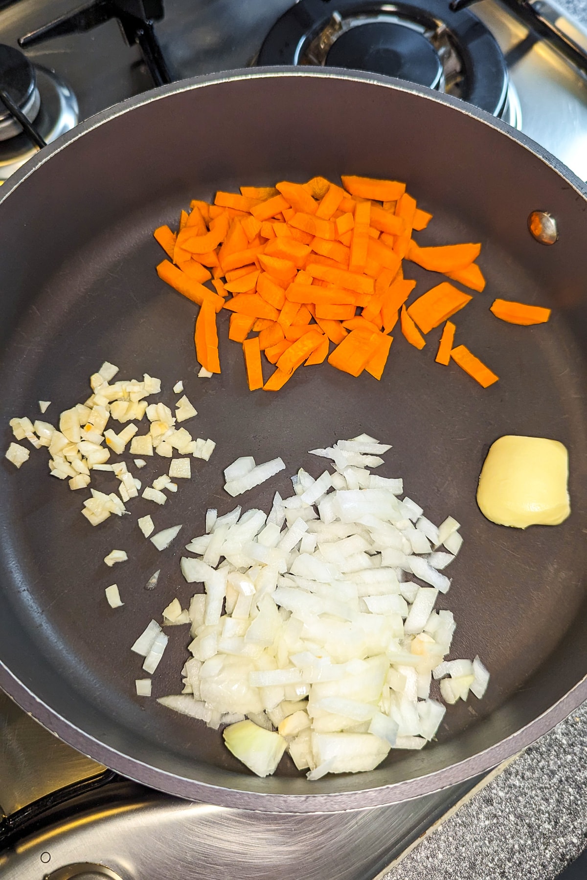 A pan with diced onions, carrots, garlic and a cube of butter.