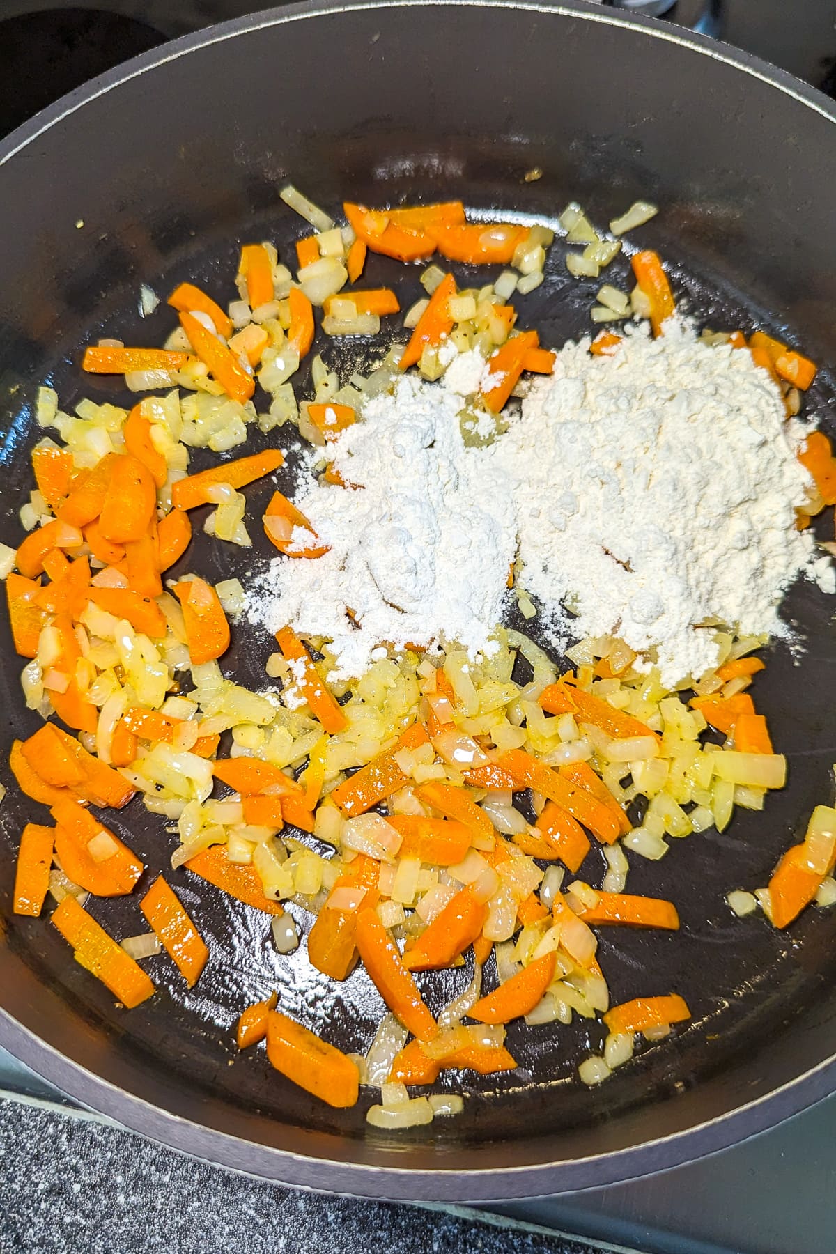 A pan with cooked onions and carrots and a little bit of all-purpose flour.