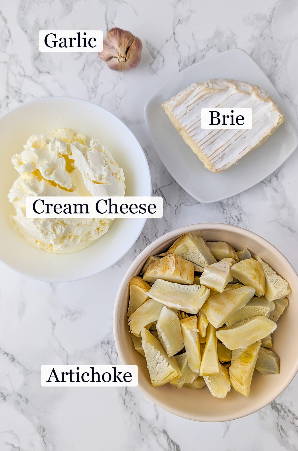 Cream cheese, artichoke, brie and garlic on a white marble surface.