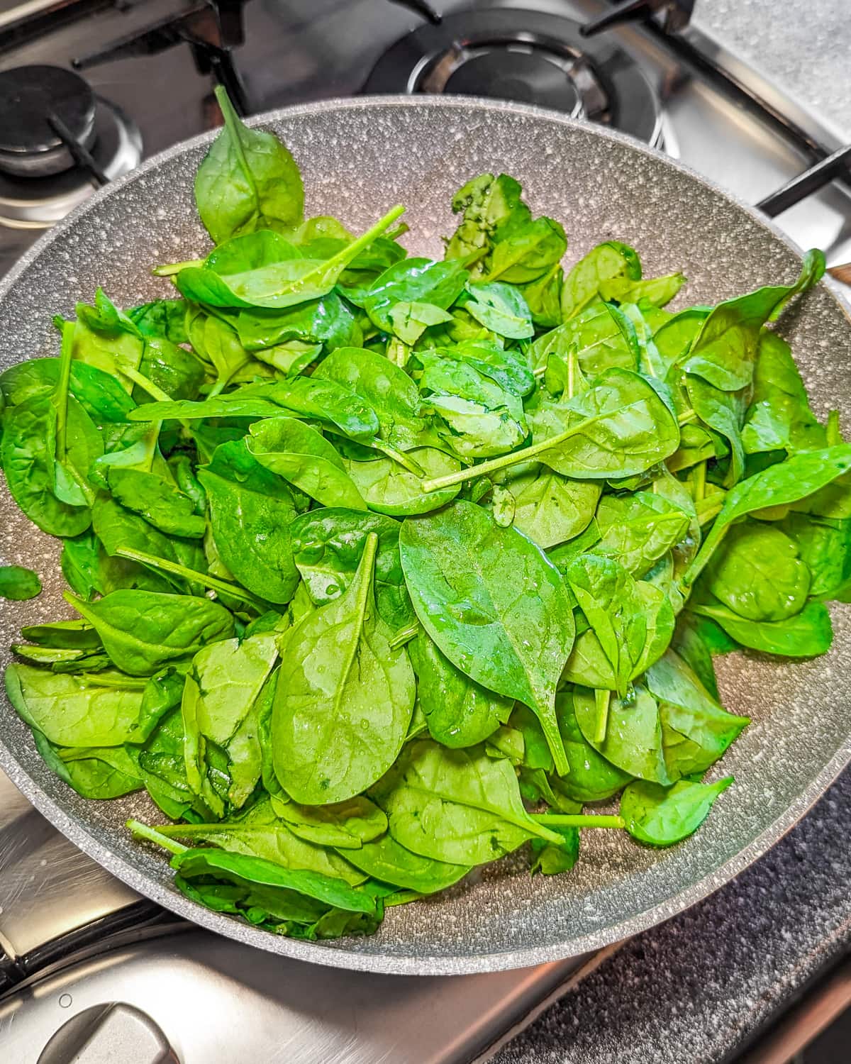 A frying pan with fresh spinach in it.