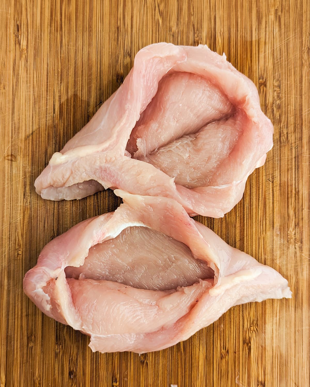 Two pockets of chicken breasts on a wooden cutting board.