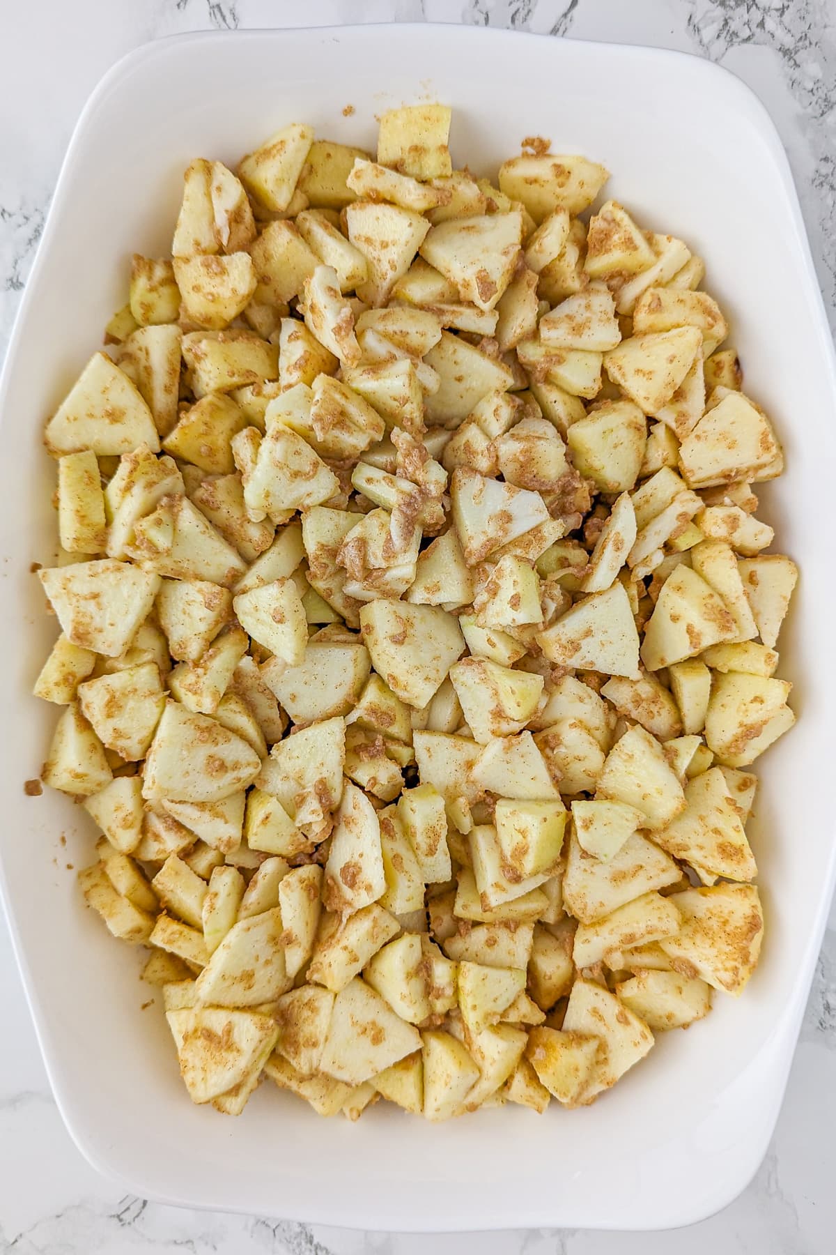 White casserole with apple triangles on a white surface.