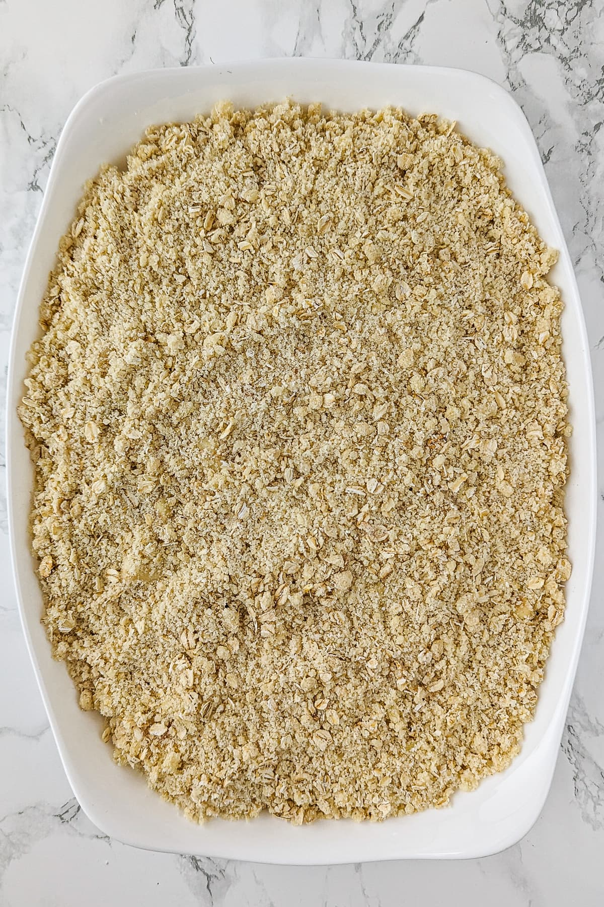 White casserole with apple crumble on a white surface.