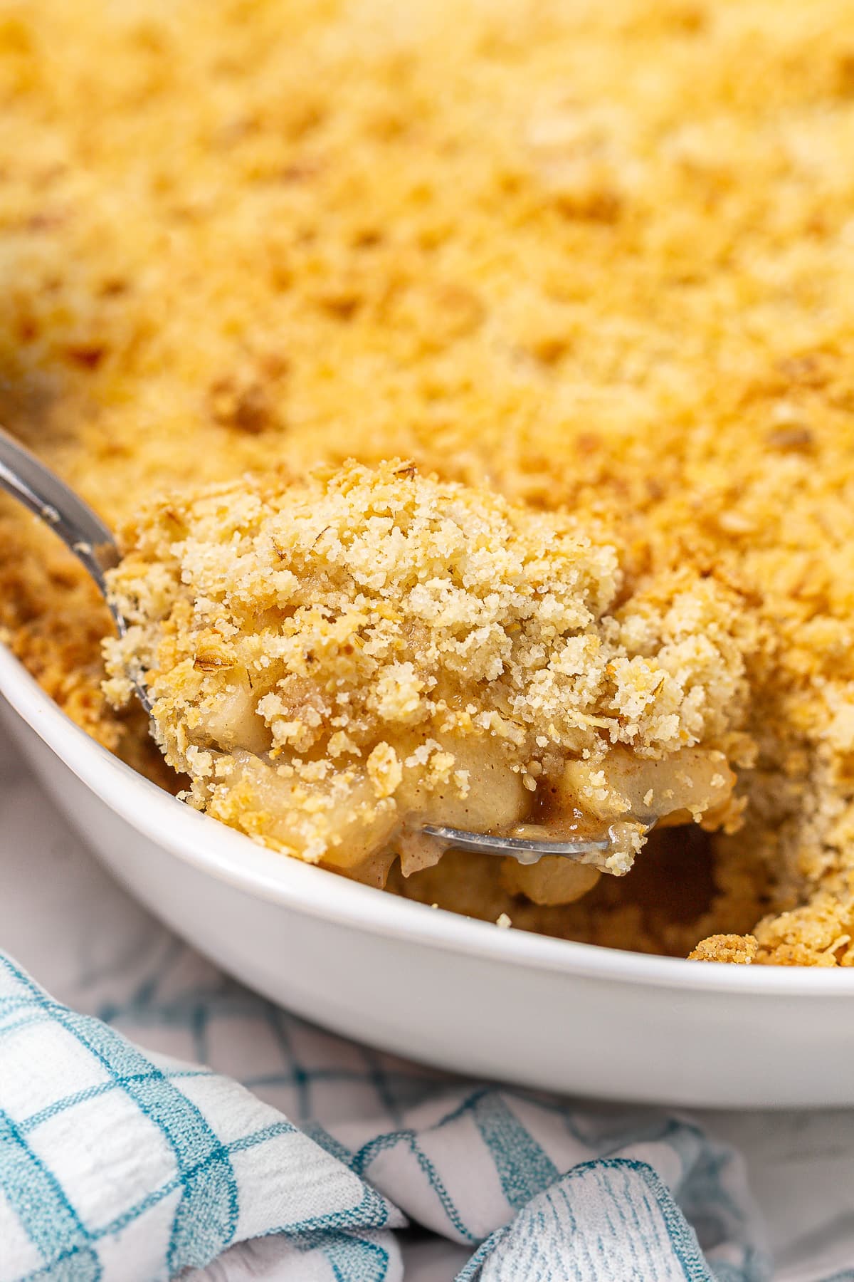 White casserole full of apple crumble with a close view of a tablespoon in it.
