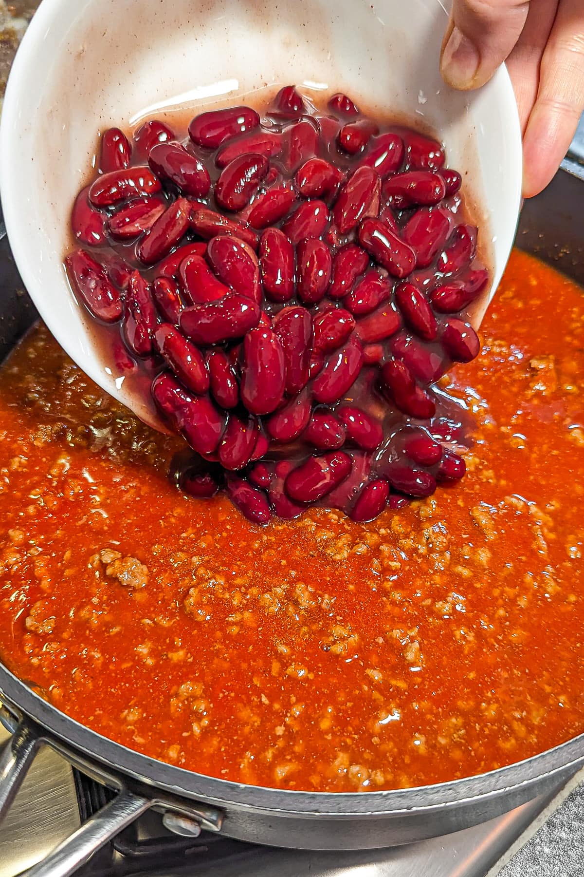 Pouring red beans in a pan with beef chili.