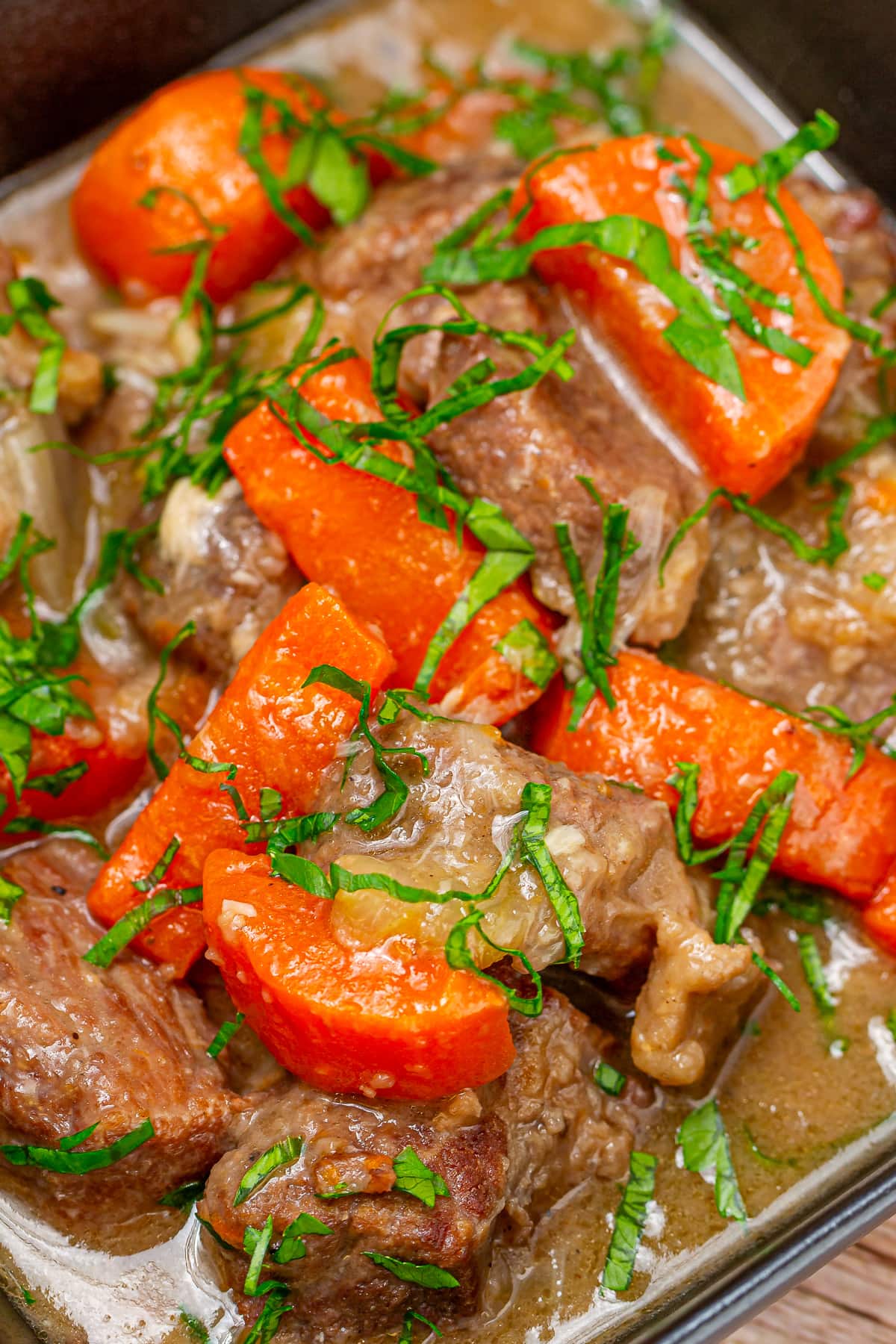Beef stew with carrots and chopped parsley in a squared black plate on a wooden surface.