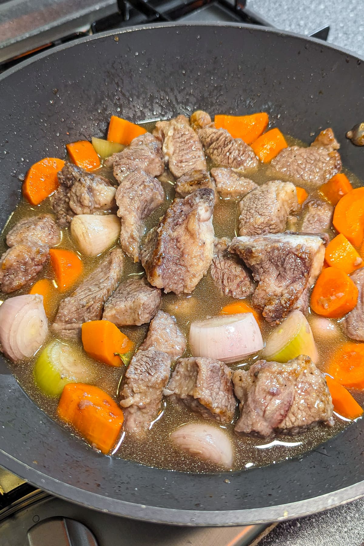 Beef stew with carrots and onions in a large wok on the stove.