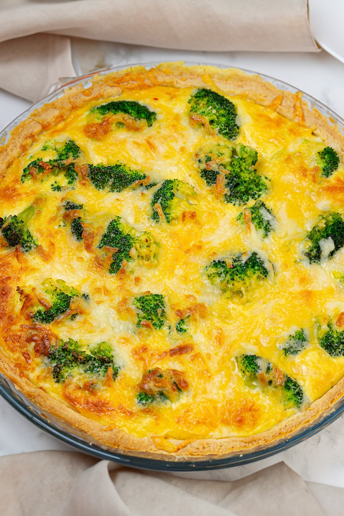 Freshly baked broccoli cheddar quiche in a glass pie dish, showing a golden-brown surface with broccoli florets and melted cheese.