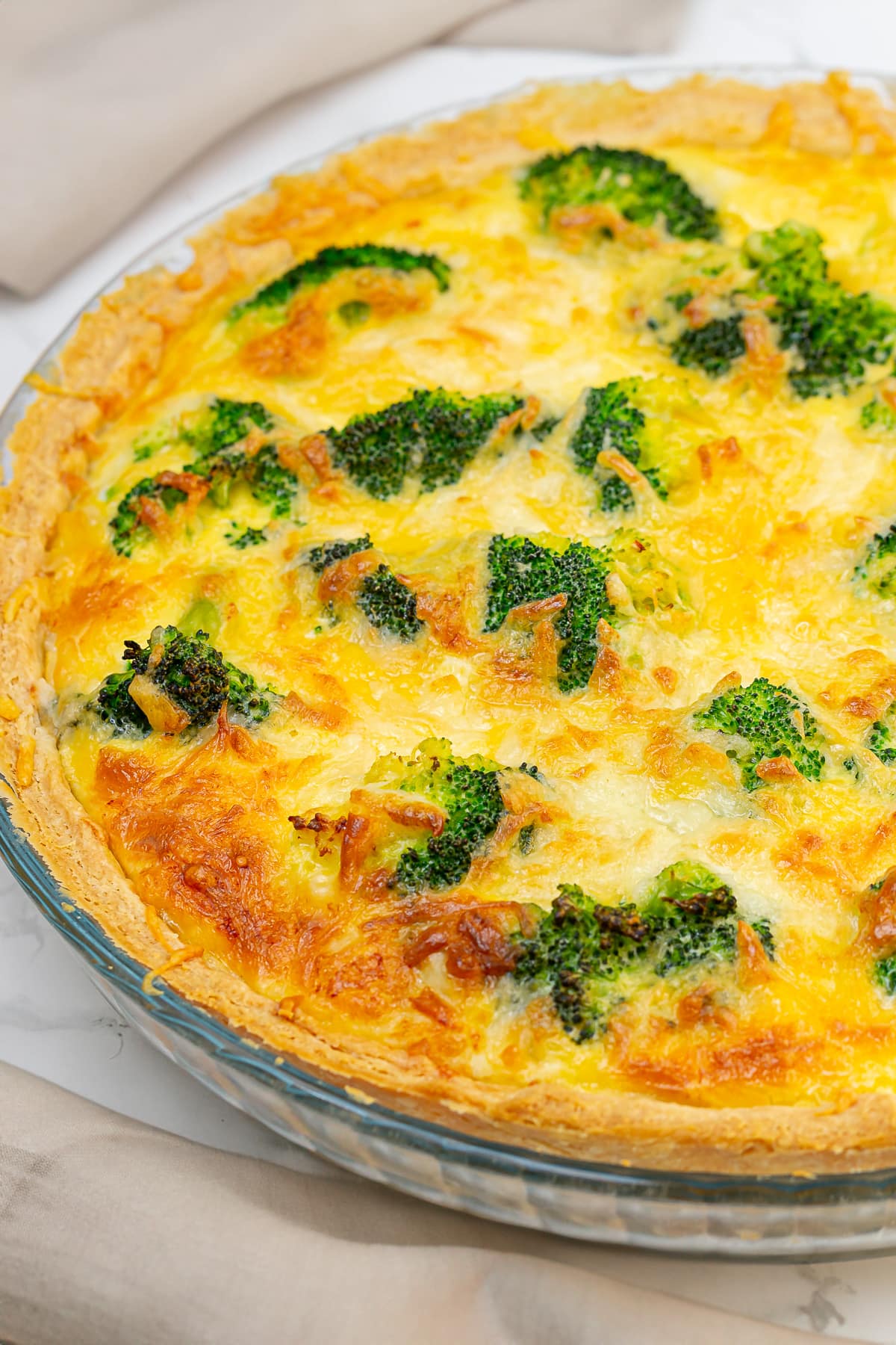 Freshly baked broccoli cheddar quiche in a glass pie dish, showing a golden-brown surface with broccoli florets and melted cheese.