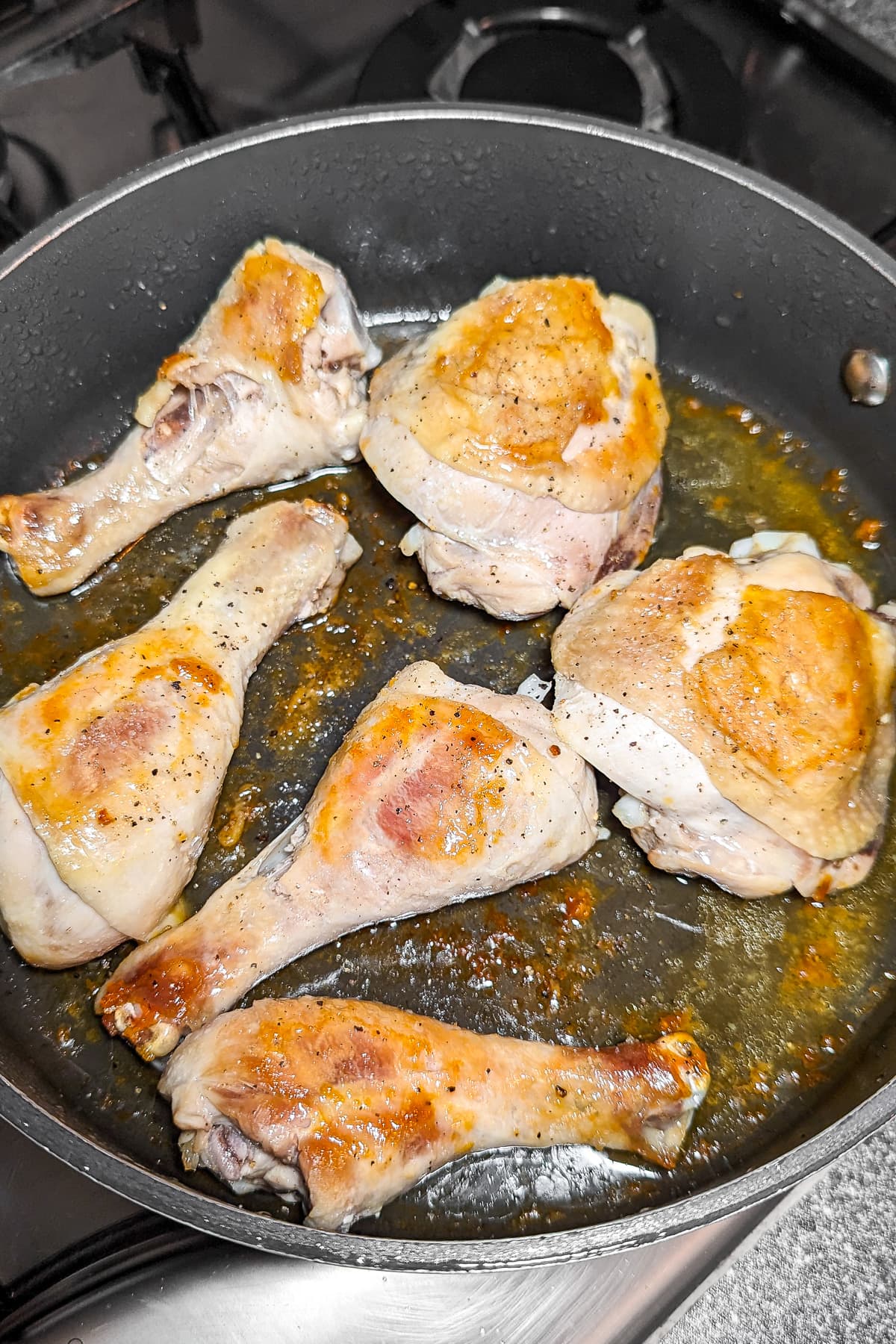 Sauce pan with fried chicken thighs and drumsticks.