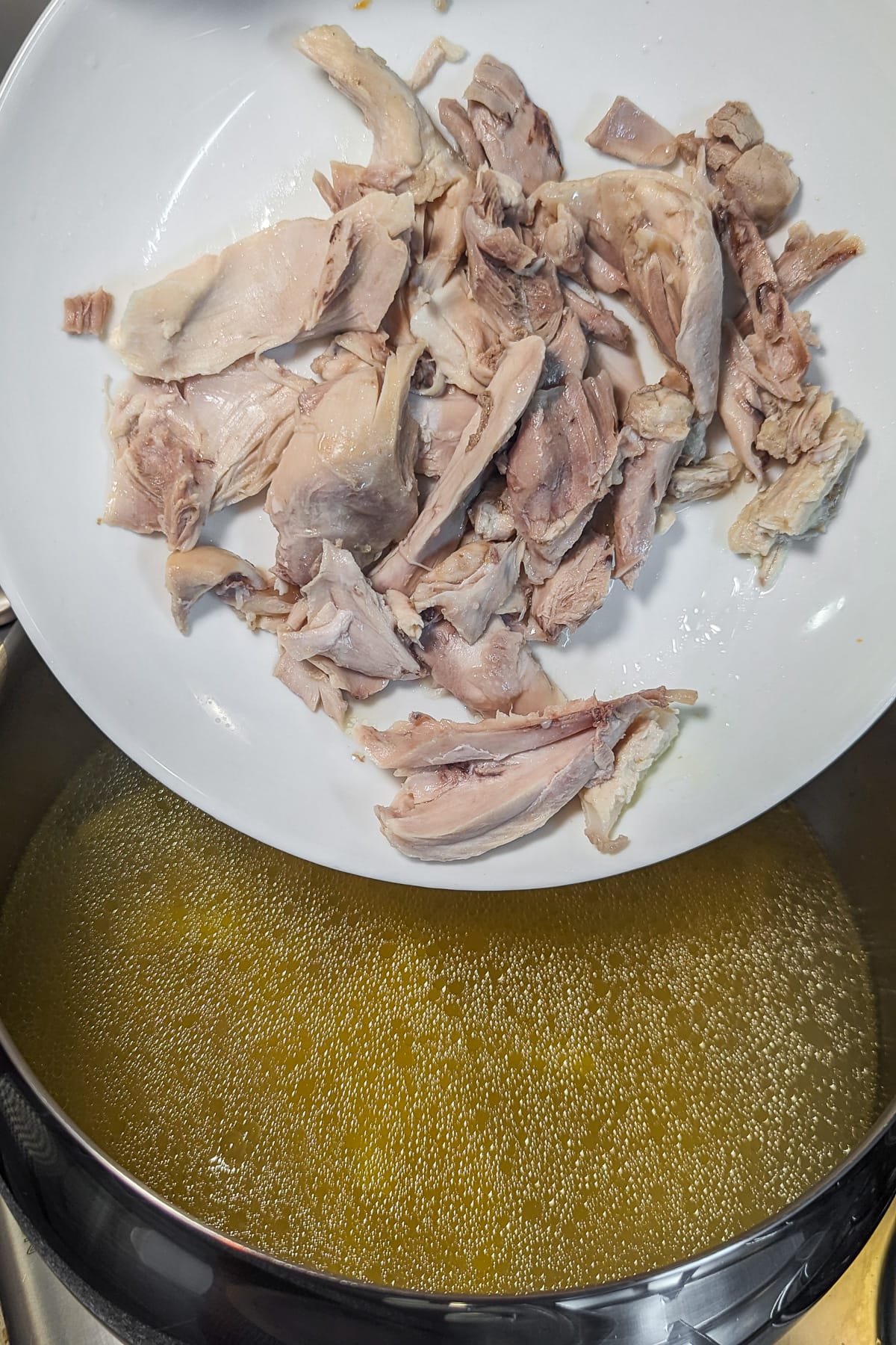 White plate with chicken meat pieces pouring in a pan with chicken broth.