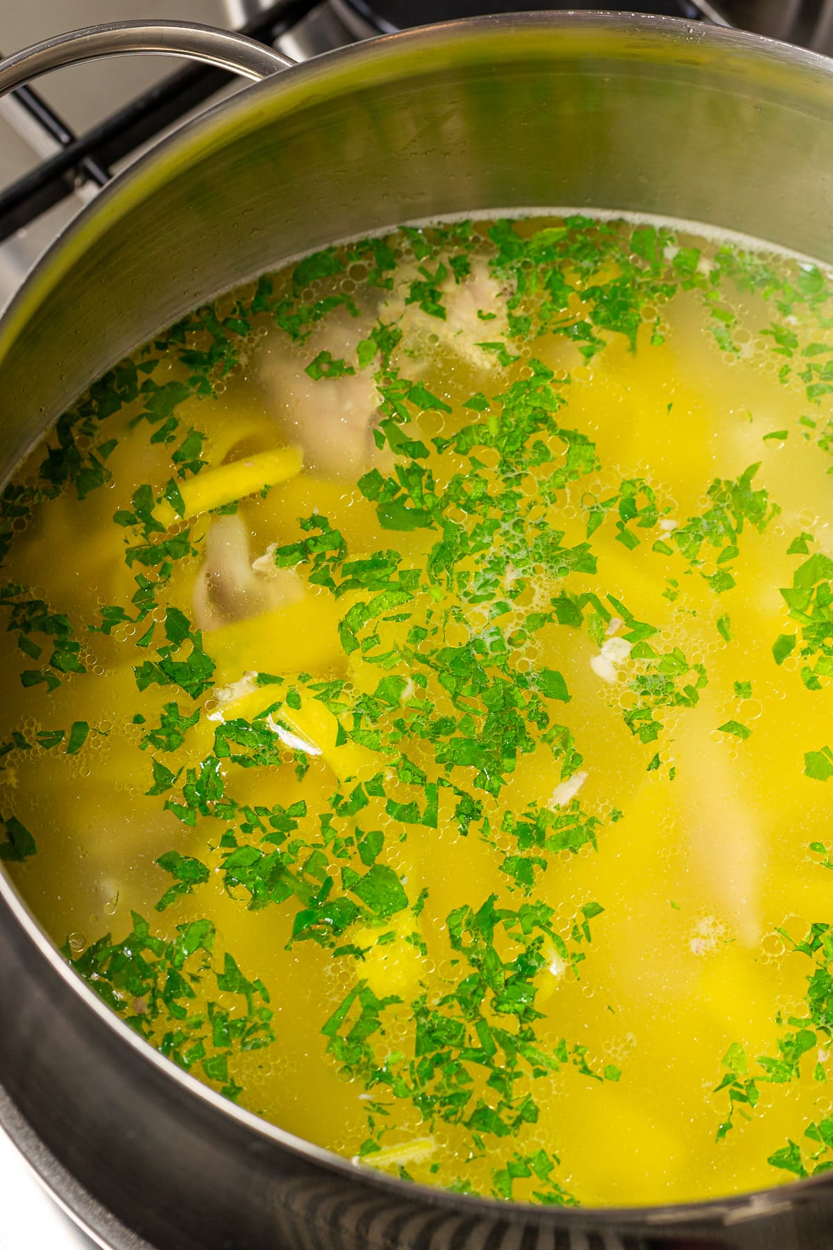 Aluminum pan with chicken noodle soup with chopped parsley.