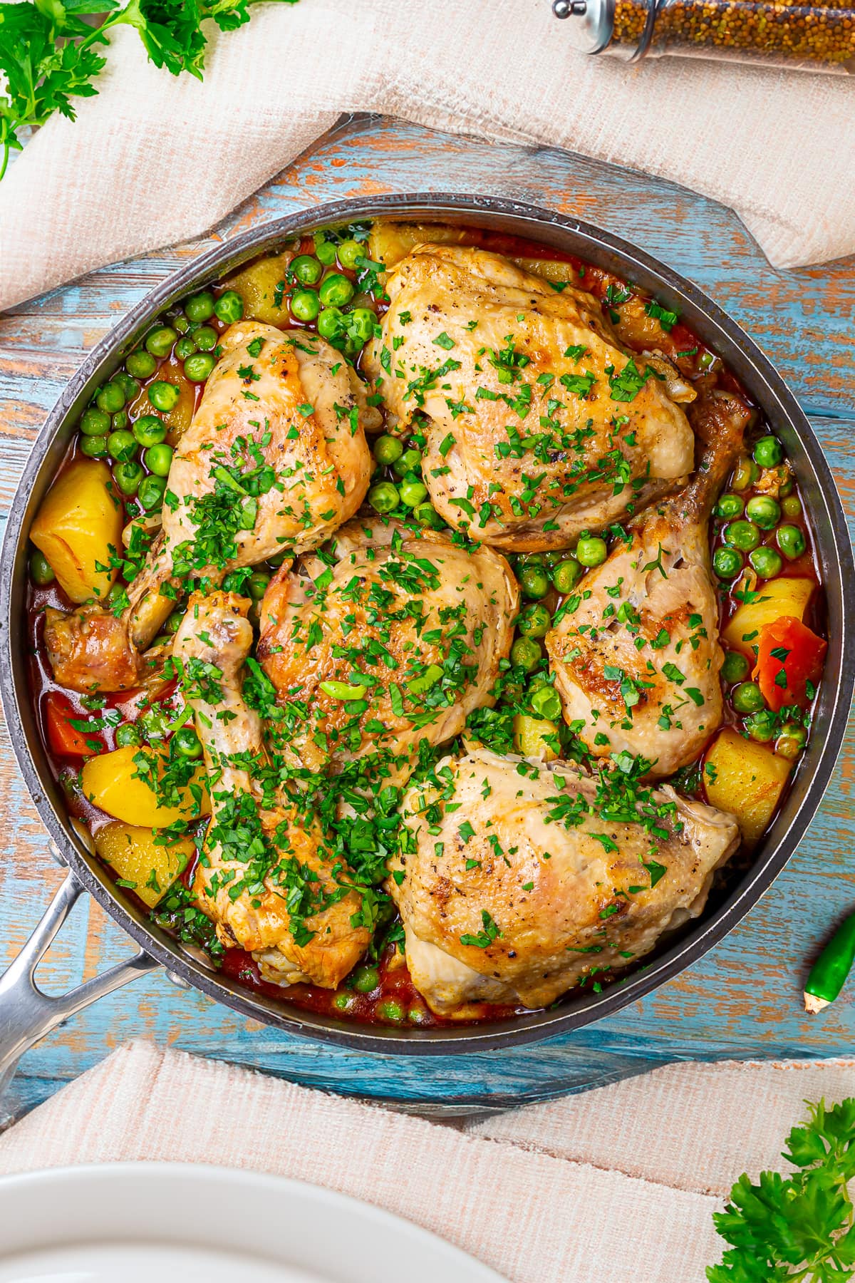 A completed chicken stew garnished with fresh chopped parsley, featuring tender chicken legs, peas, carrots, and potatoes in a rich broth.