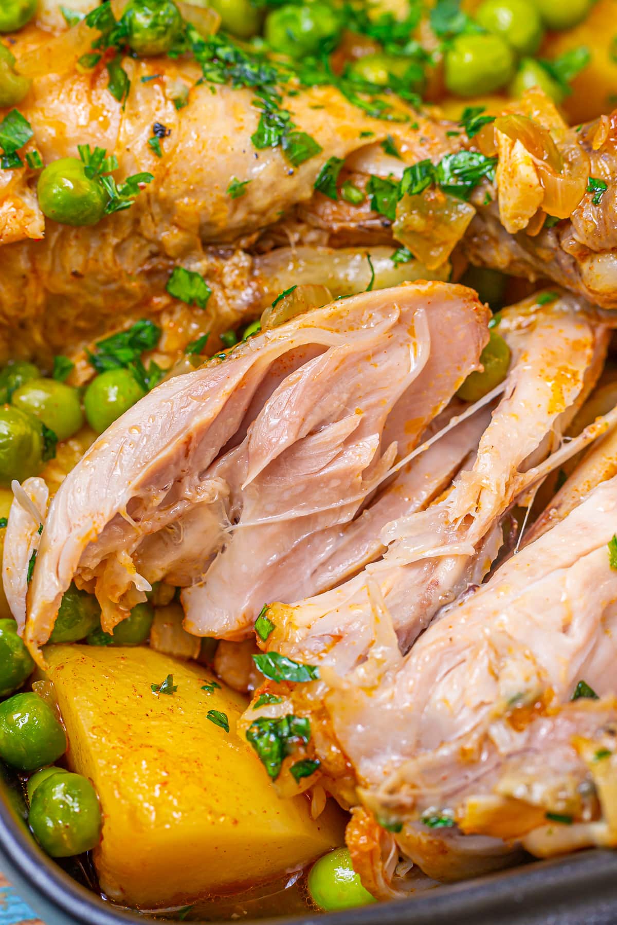 A close-up showing the texture and juiciness of the chicken stew, highlighting the succulent pieces of chicken, vibrant green peas, and yellow potatoes.